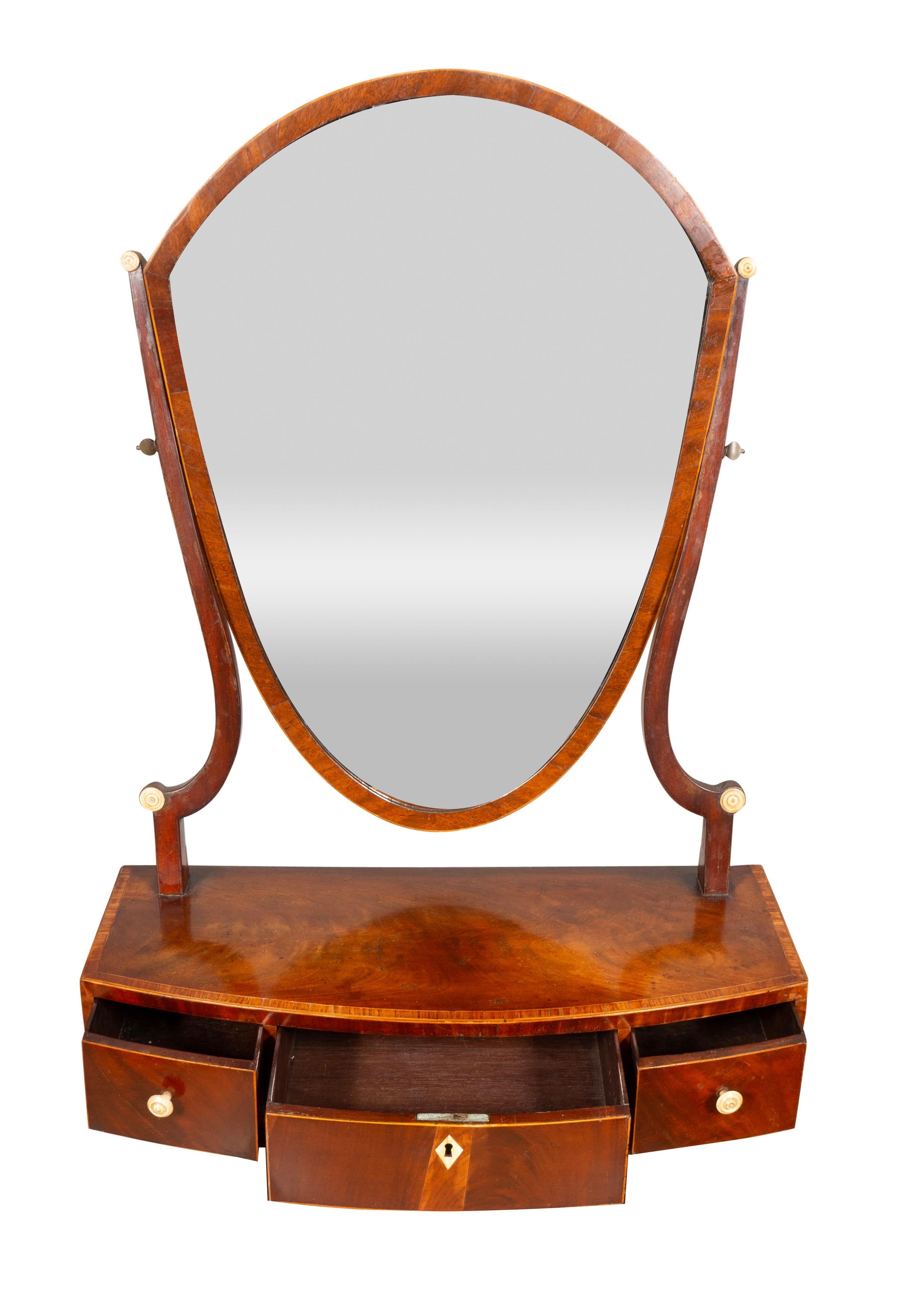 With a shield shape mirror with two supports to enable adjustment. The bow front cross banded  base with drawers. Ball feet. Typically a bedroom piece to place on a chest of drawers.