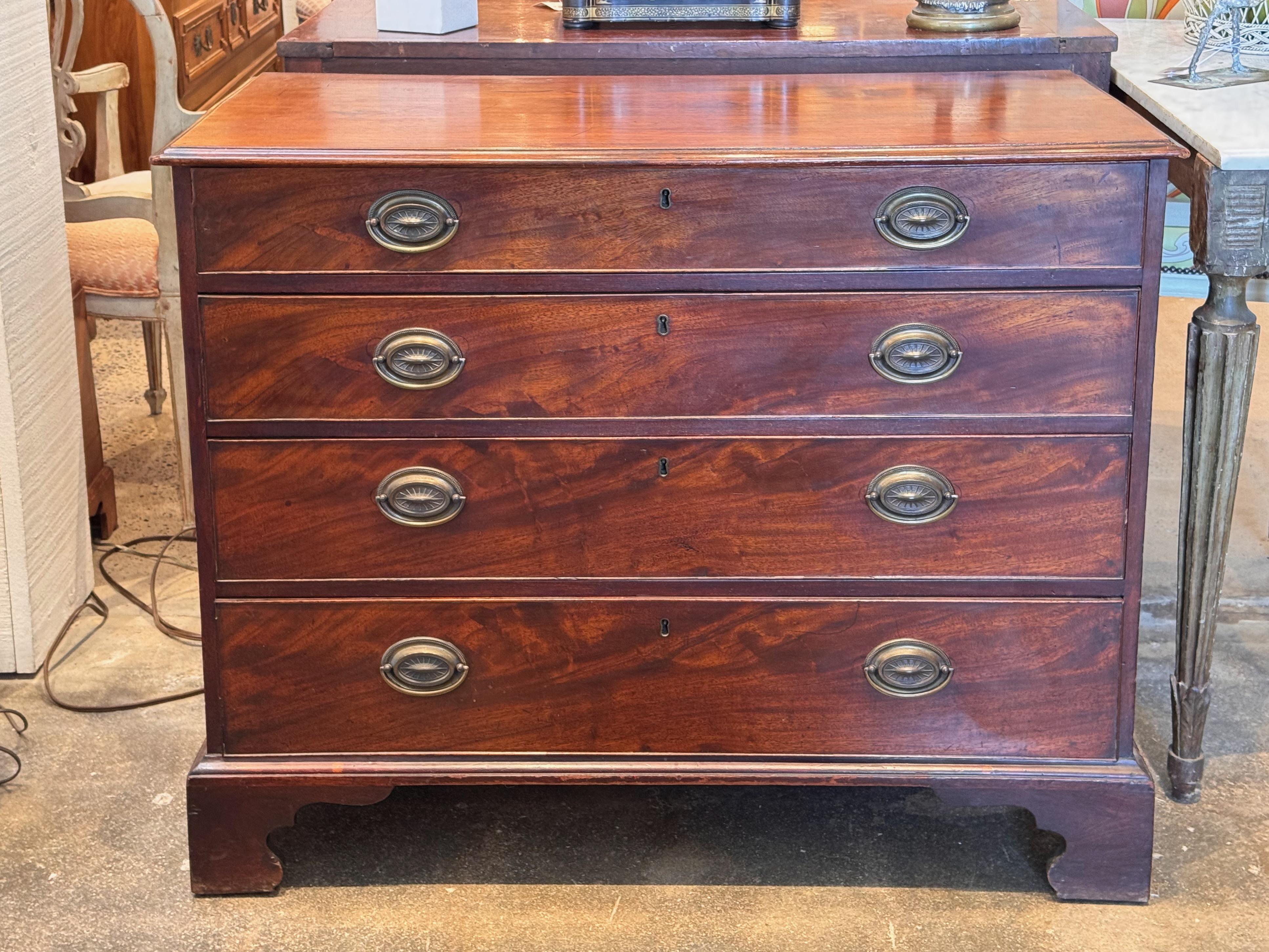 Late 18th to early 19th century George III mahogany chest featuring four graduated drawers, each with brass oval backplate pulls and keyholes. The case rests on shaped bracket feet, with a molded top and clean linear profile. Dovetailed drawer