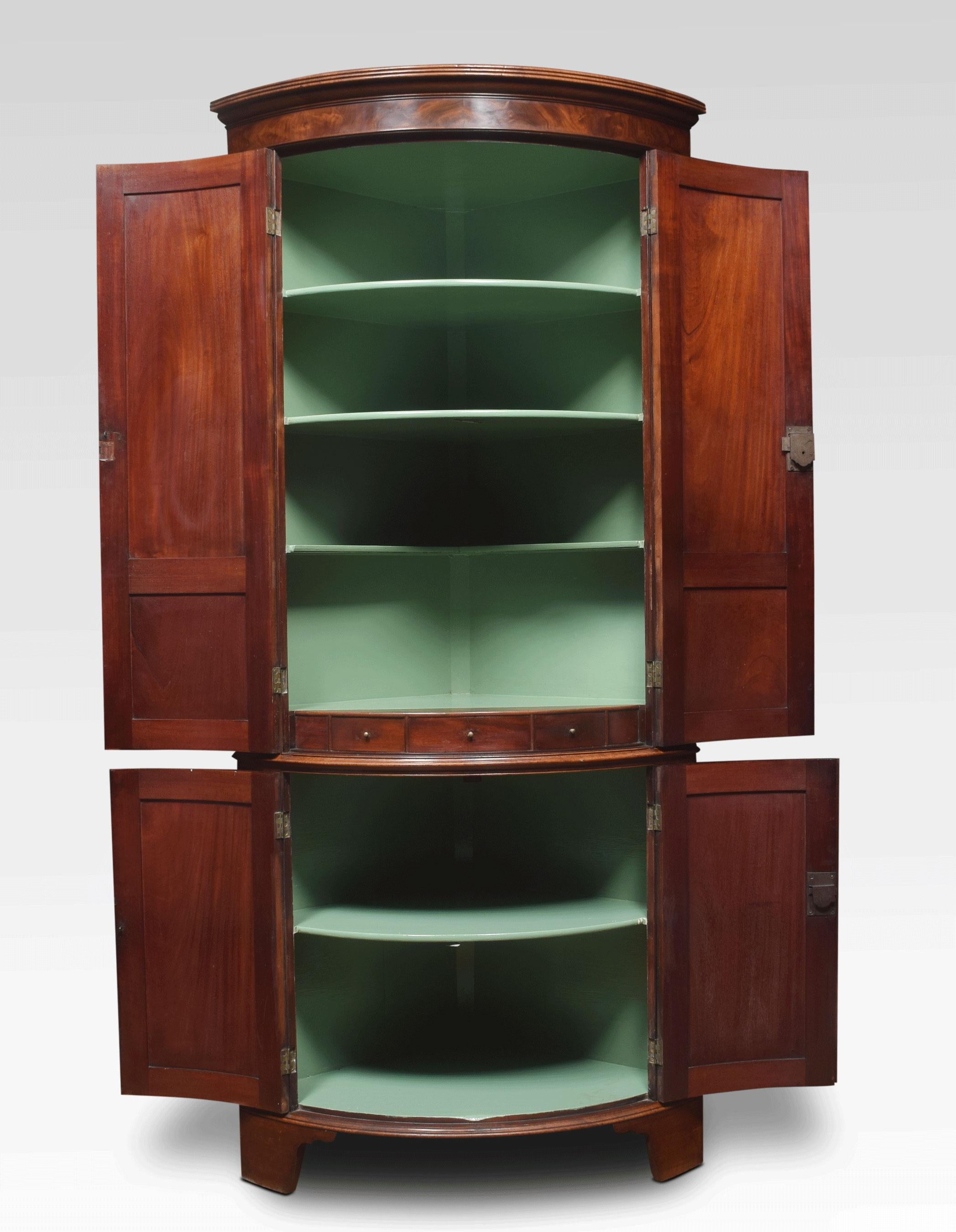 Early 19th century George III mahogany floor standing corner cabinet. The molded cornice above a pair of flame paneled doors enclosing a shelved interior with three short drawers below. The base section with similar panel doors, all raised up on