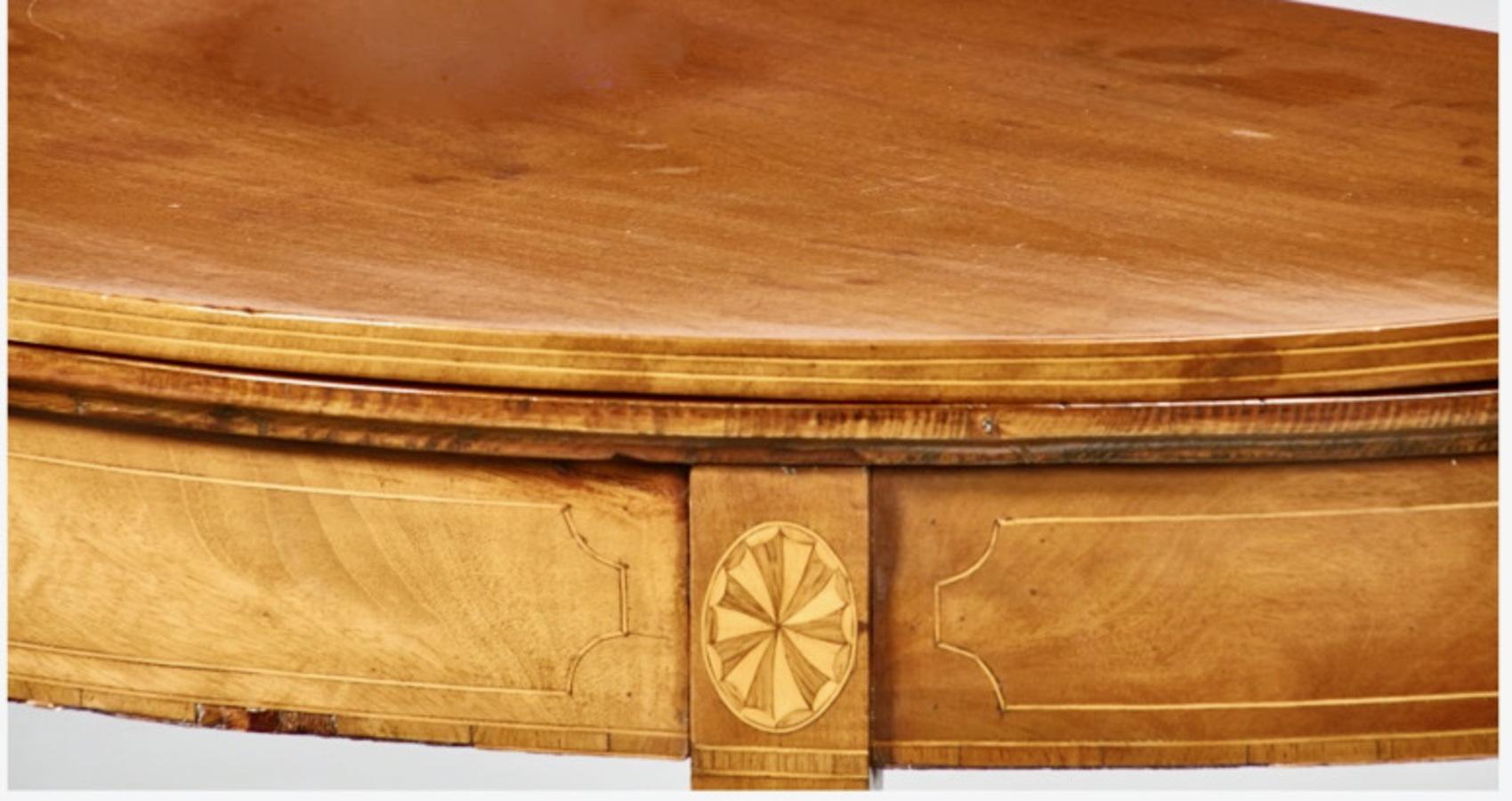 This is a good example of a George III, late 18th century mahogany fold-over demi-lune games table. The table features satinwood line inlay, a solid mahogany fold-over top, inlaid paterae at all four legs with line inlay to the skirt and legs. The
