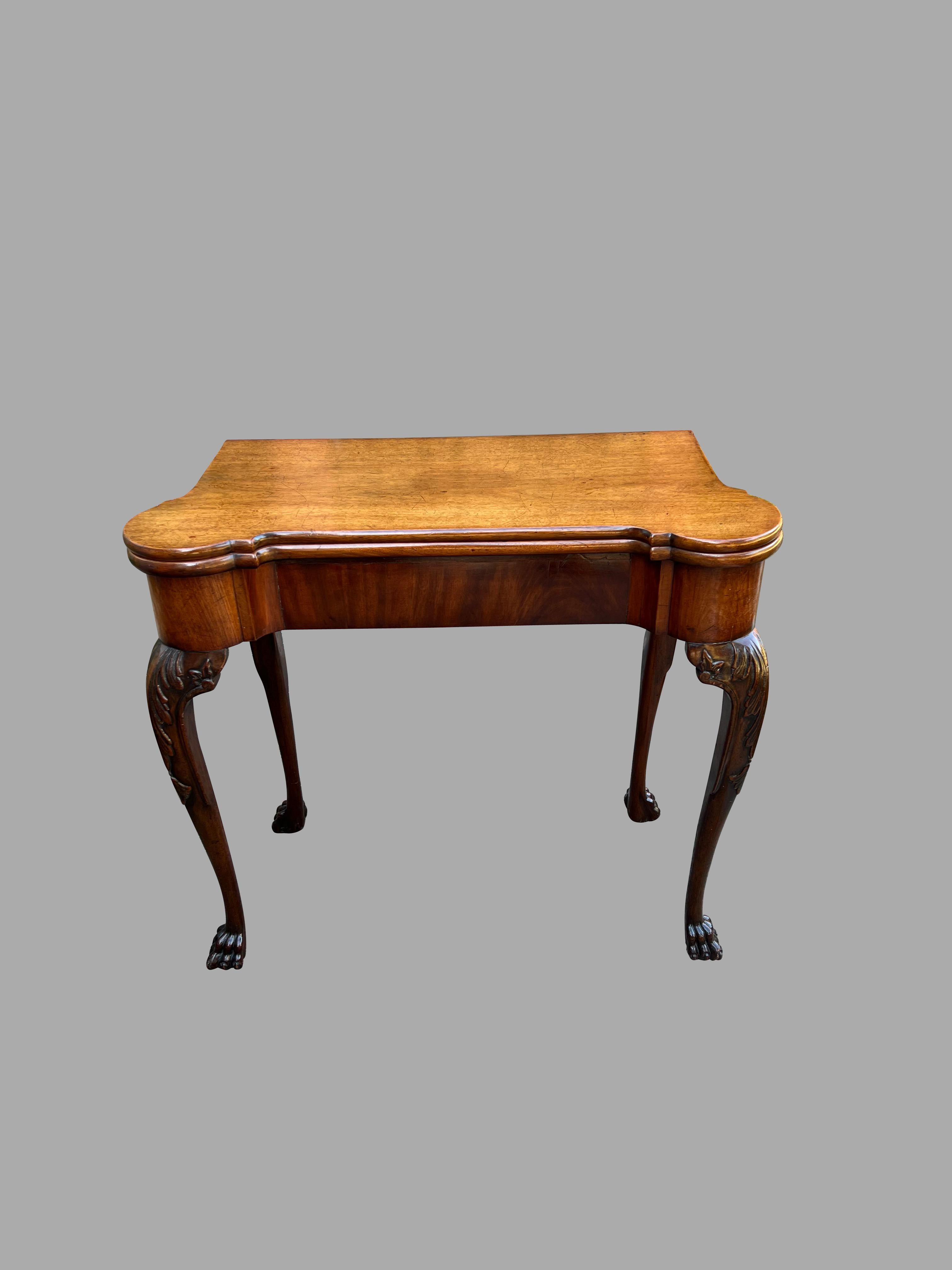 A good George II period mahogany card table, the shaped top over carved cabriole legs ending in hairy paw feet. The top, when opened, retains an old baize cover with 4 wells for markers, the corners designed to support candlesticks. Old finish.