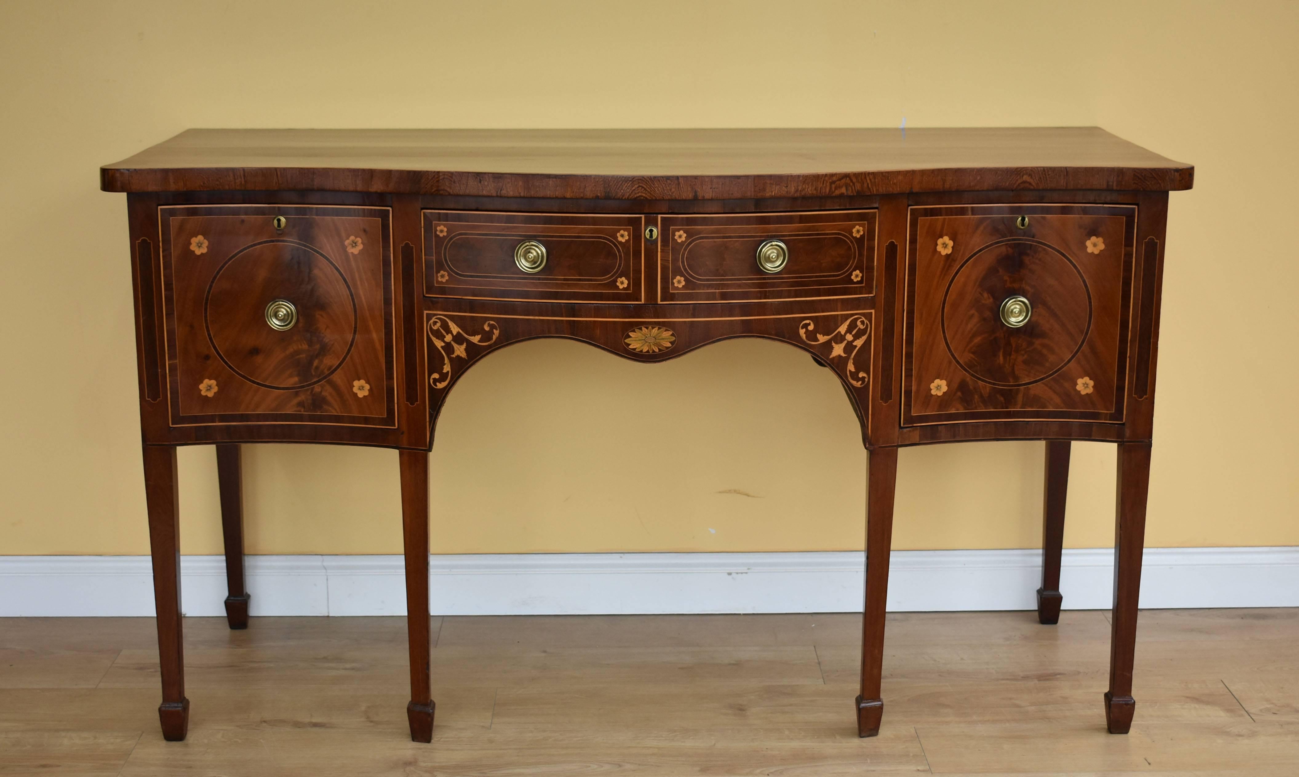 For sale is a fine quality George III mahogany and inlaid serpentine sideboard. The top with broad zebra wood banding above three drawers, each with strung decoration and flower head inlays. The right hand drawer has its original cellaret, over six