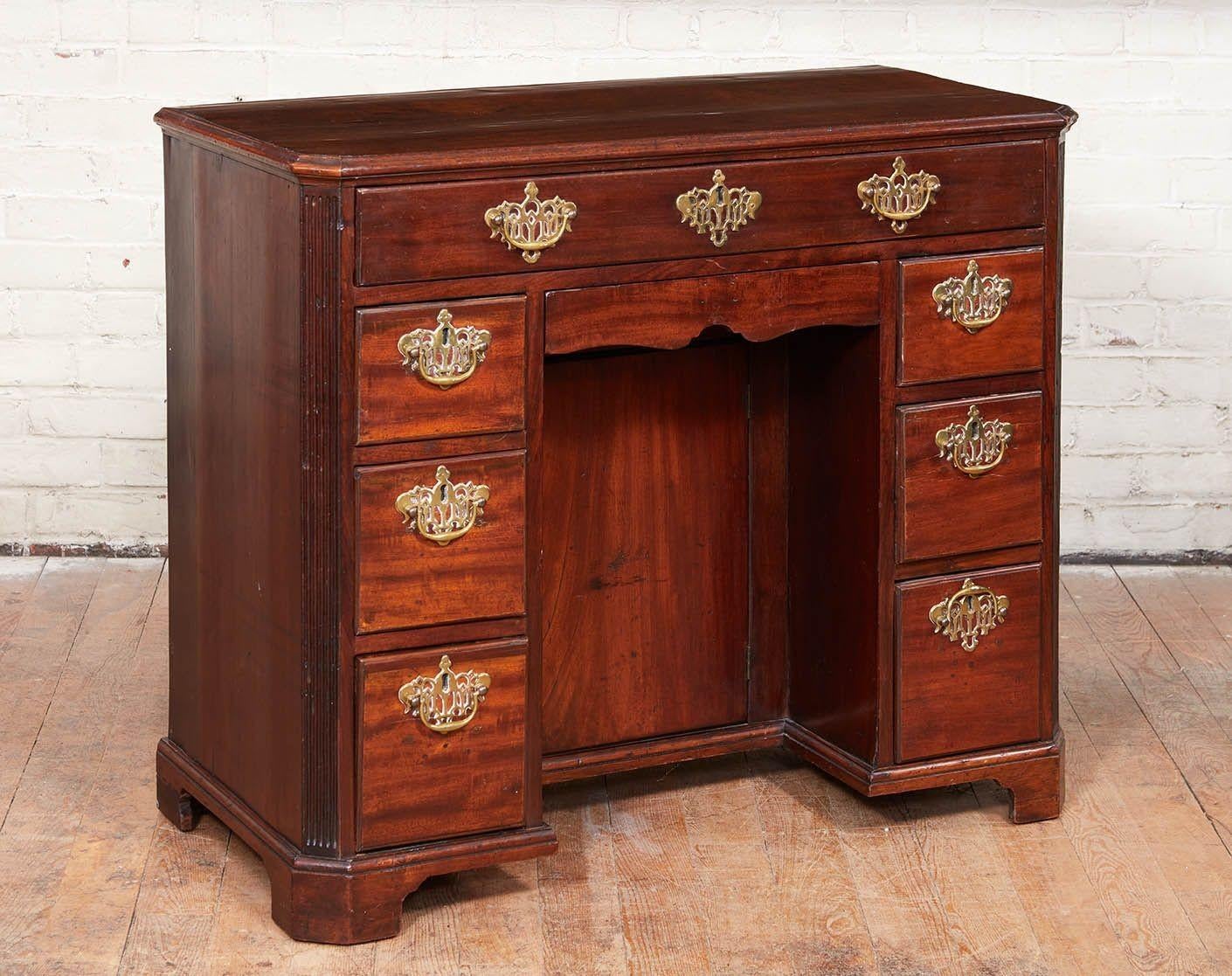 Fine George III period mahogany kneehole desk having richly grained top with canted corners and molded edge, the long drawer flanked by two rows of short drawers with door in recess, the canted corners with fluted rails and standing on original