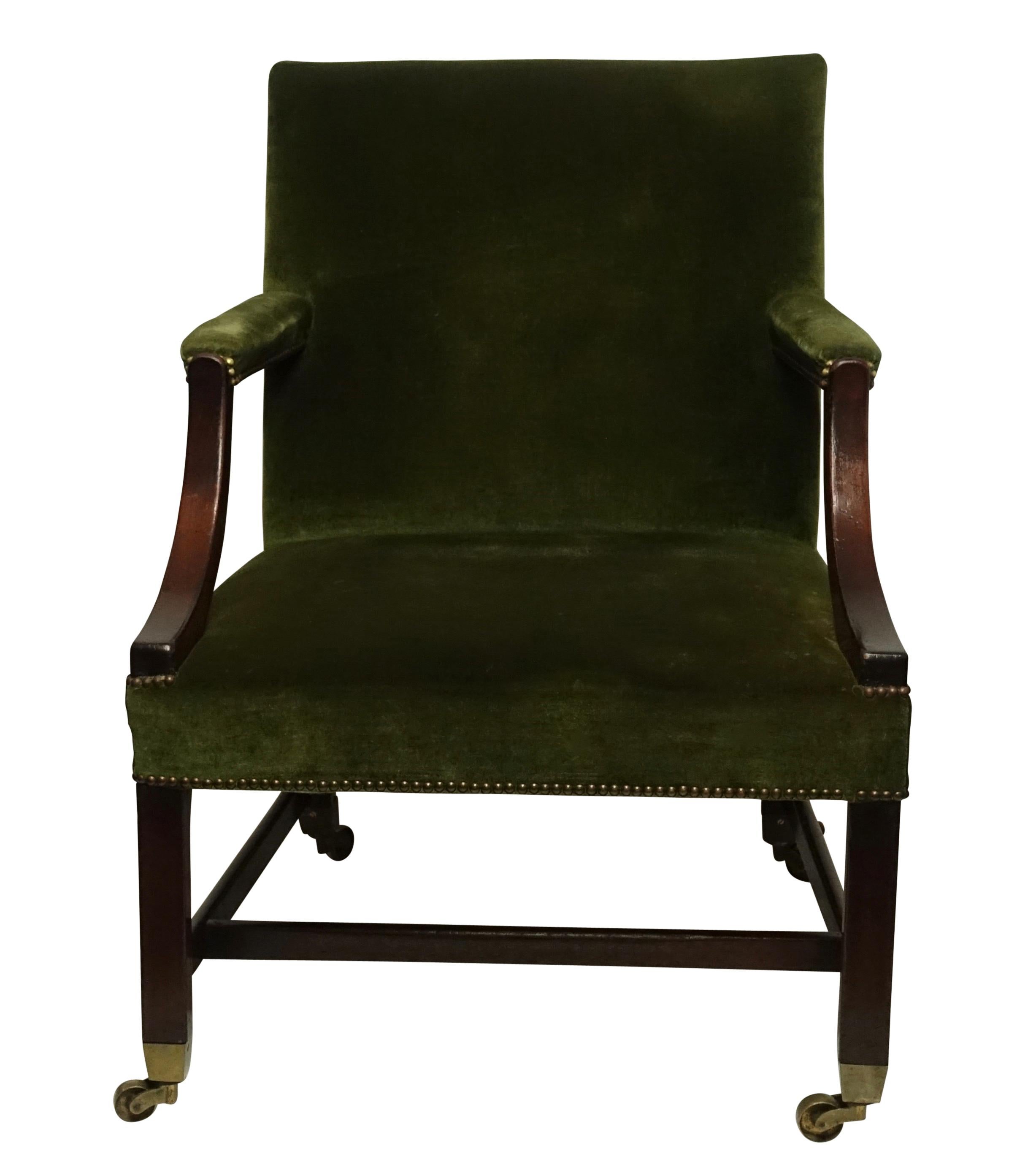 A commodious Georgian style mahogany library armchair with down swept arms, brass tacking accenting the vintage mohair upholstery, the square beam legs ending in substantial brass cup and caster feet. England, circa 1780.