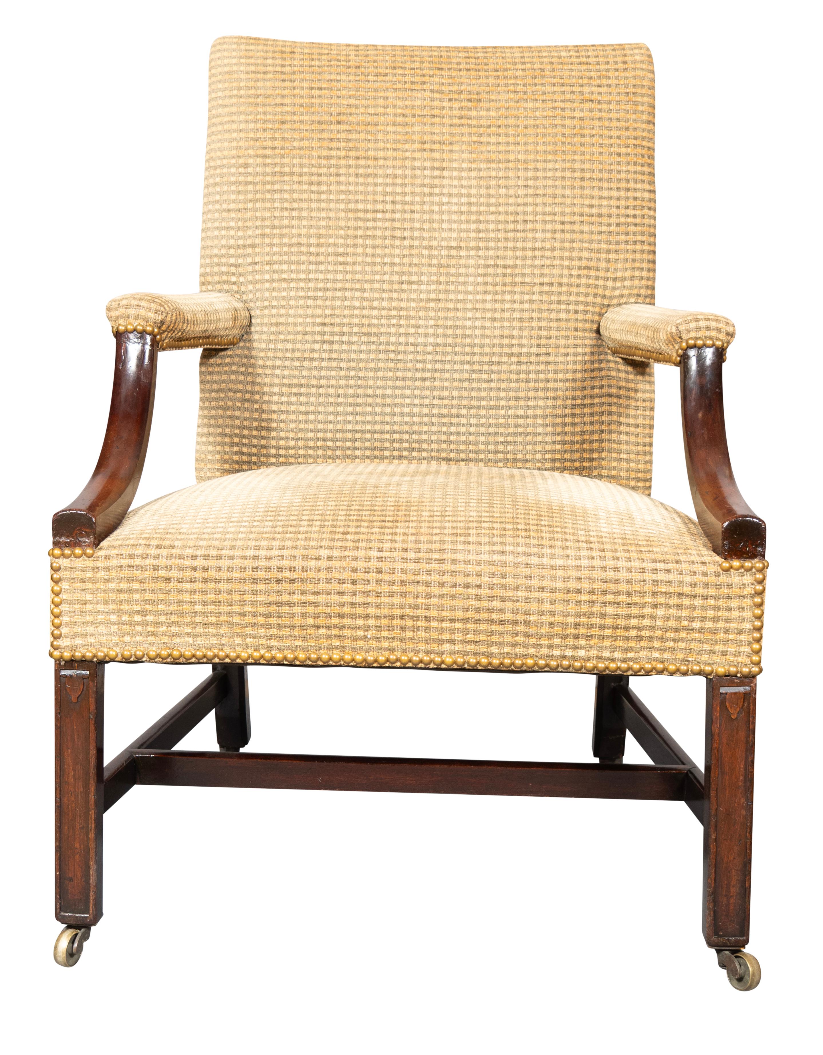With square upholstered back and seat with down swept partially upholstered arms with square section legs with raised border and lappet carving at top of leg. H form stretchers. Brass casters.