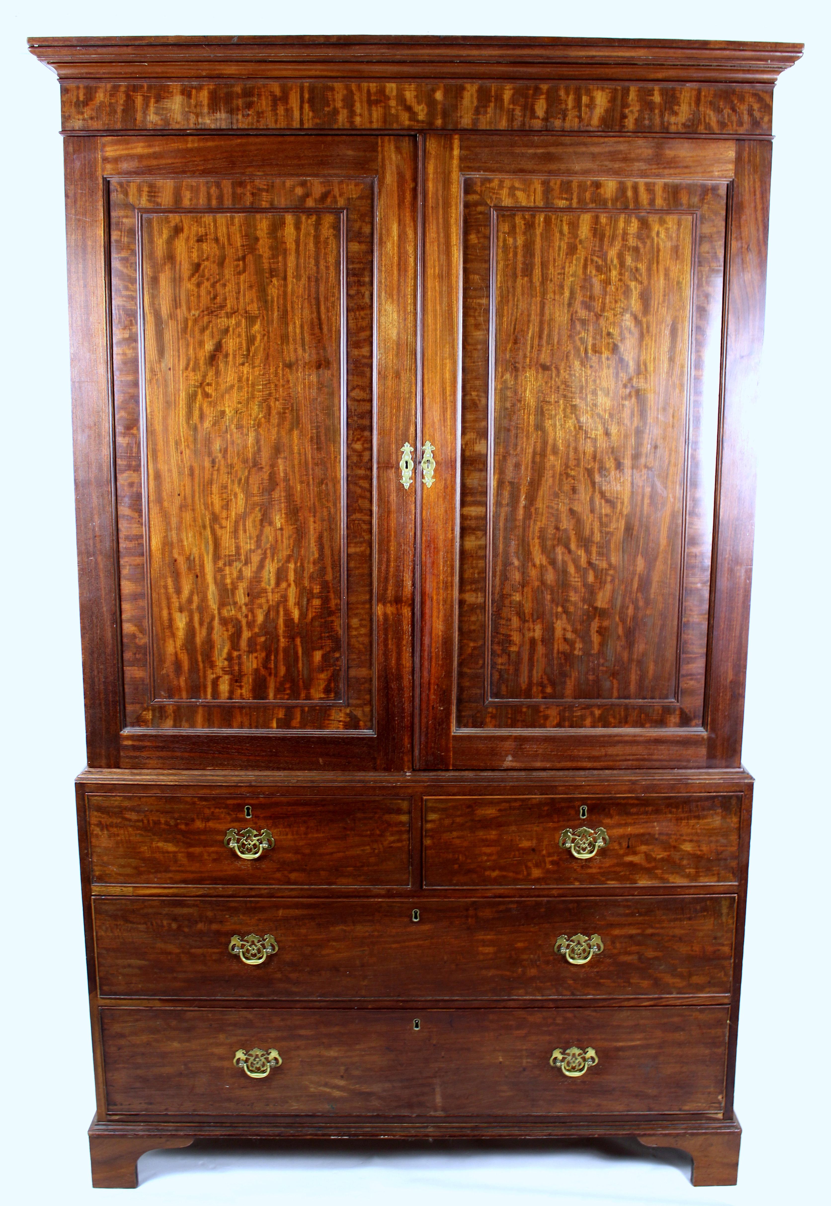 This handsome and well-proportioned George III mahogany linen press features 2 crossbanded panelled doors which reveal a central slide over 2 short and 2 long drawers. The unit also has ornate brass hardware and is supported on bracket feet. It