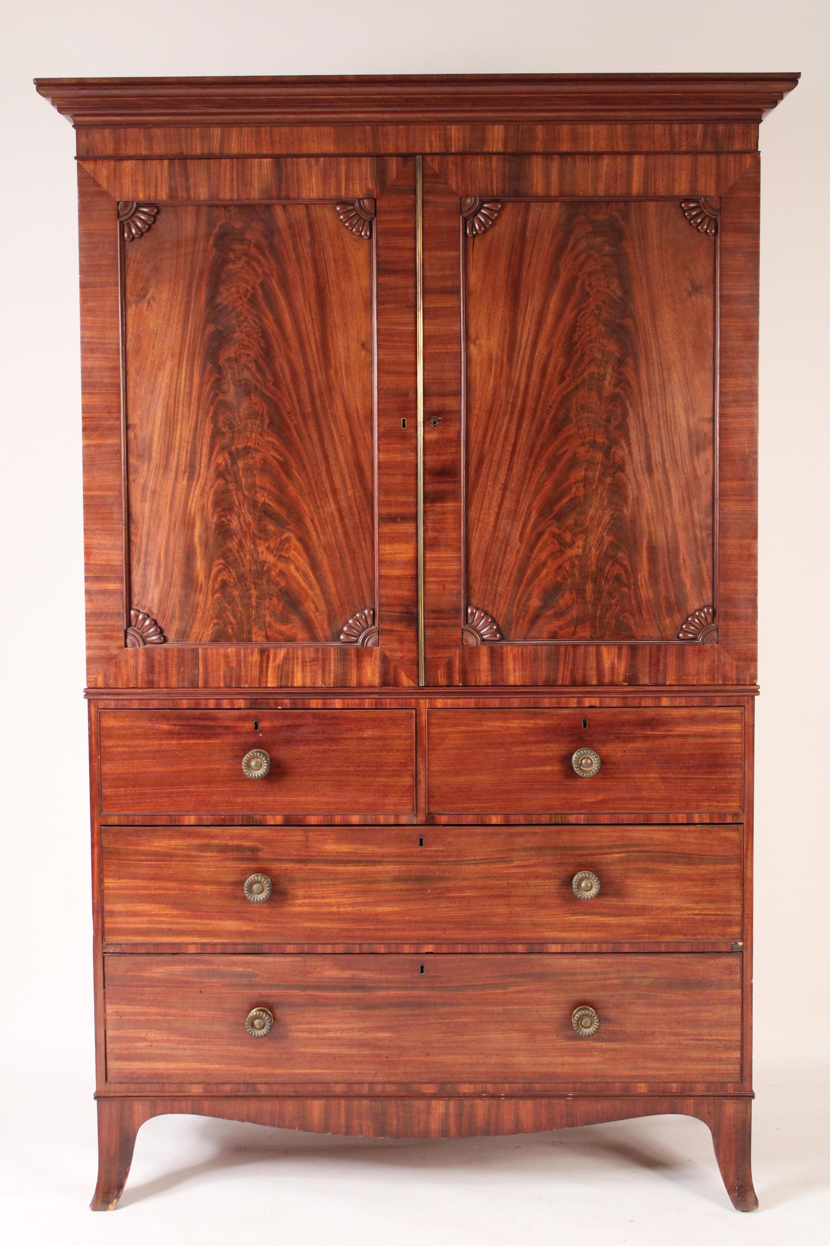 George III Scottish mahogany linen press, early 19th century. With a cove shaped pediment, two flame mahogany doors with shell carved spandrels, the interior of the upper section with 5 drawers, the bottom section with two upper drawers and two