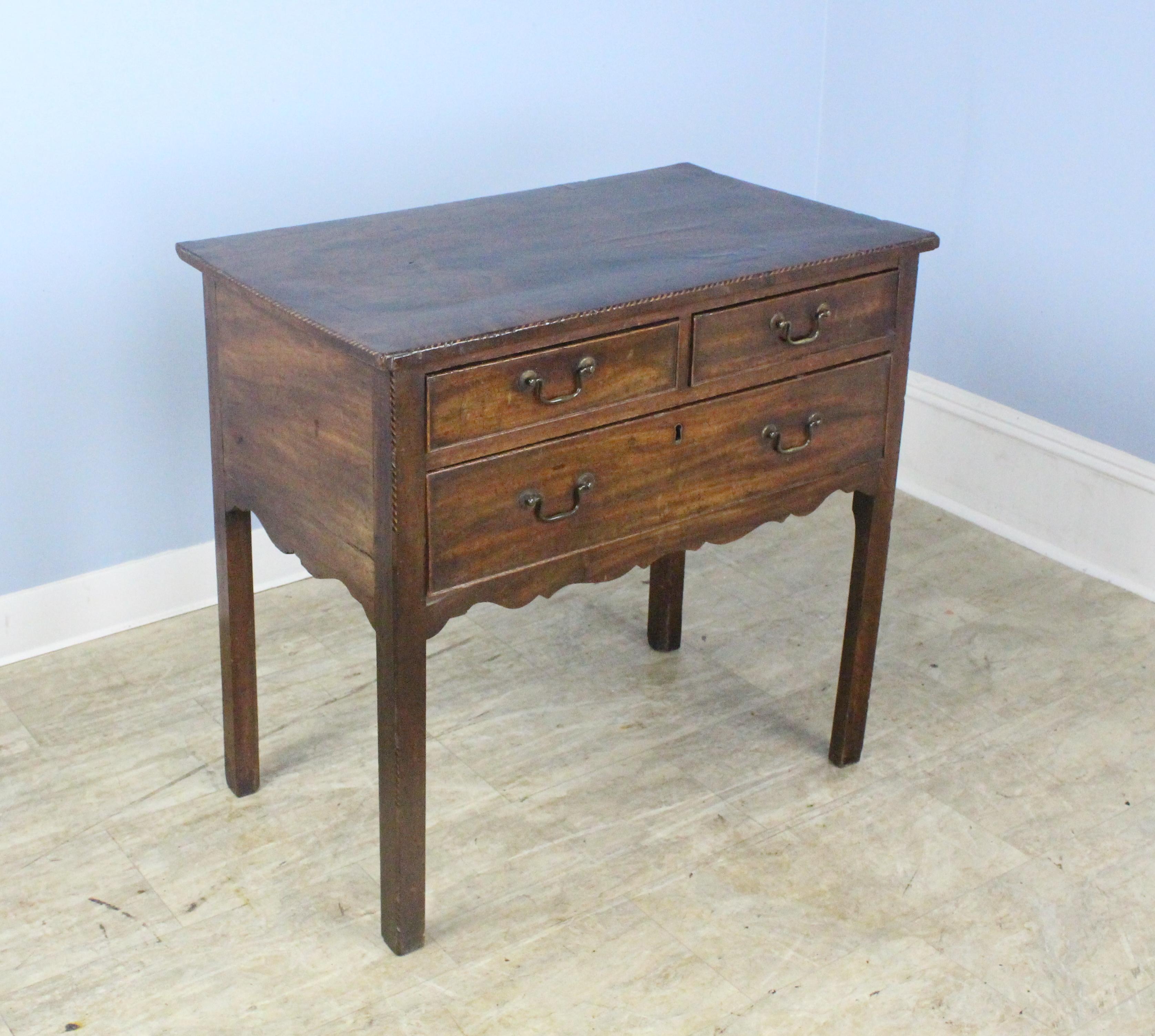 An early lowboy with a veneered rosewood top, intricate ebony and satinwood stringing, and a fancifully carved apron, all in fabulous original distressed condition. The cockbeaded drawers and original brass hardware complete the look. The bottom