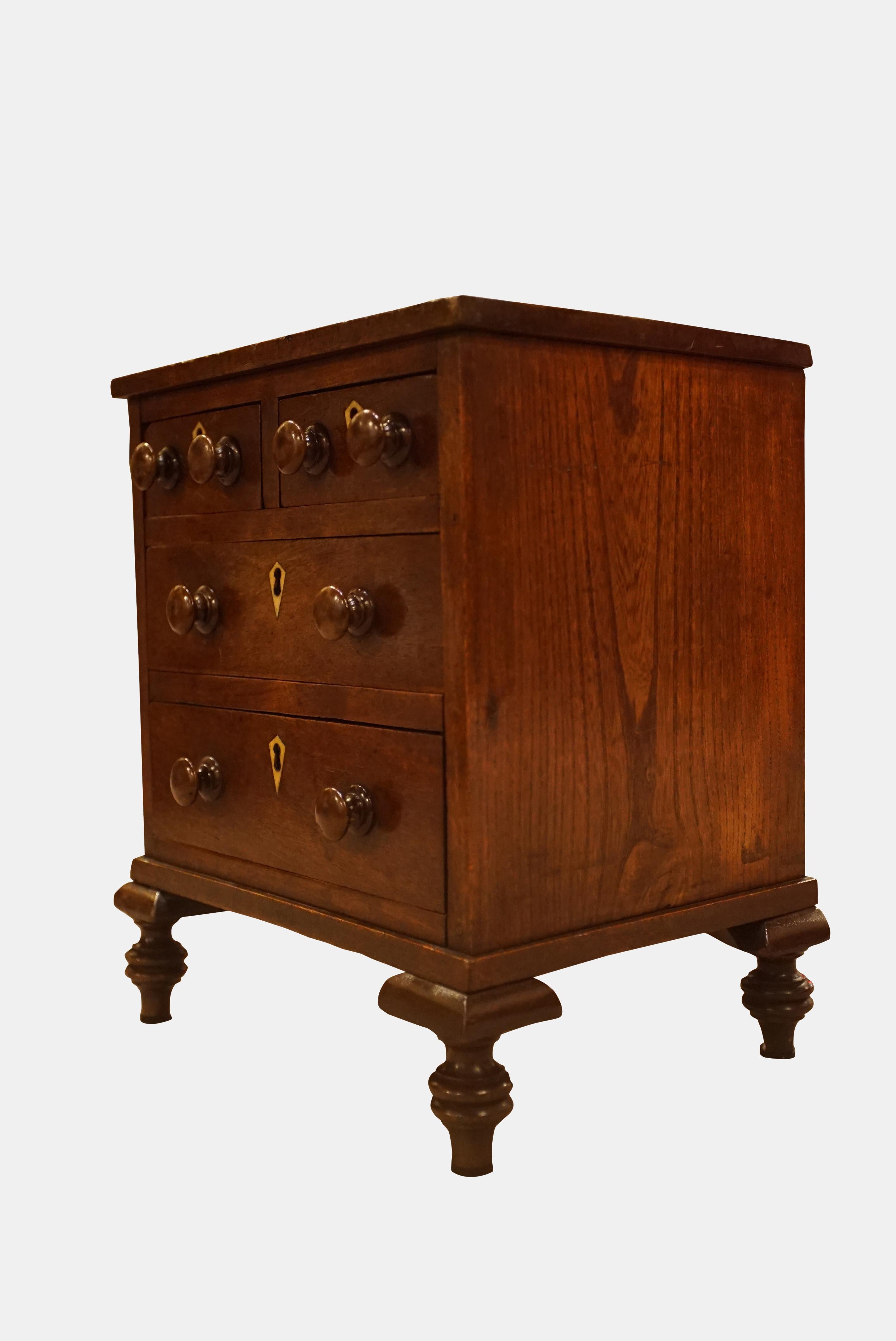 A George III Mahogany Miniature chest of drawers with turned pulls, ivory escutcheons, raised on turned feet.