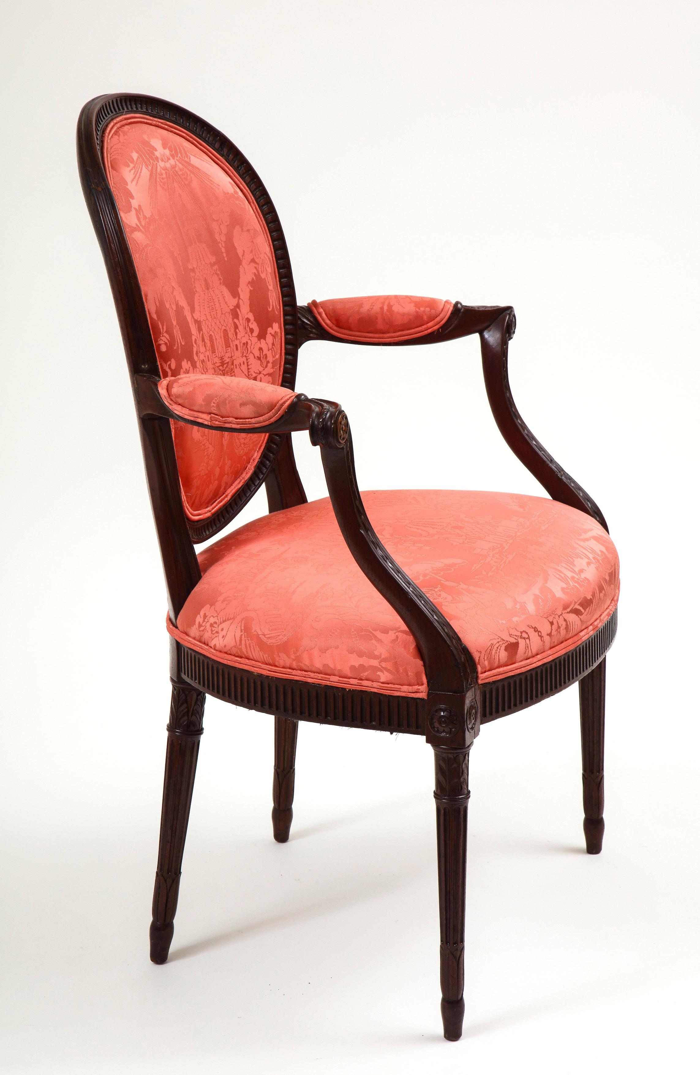 Upholstered in a chinoiserie red silk damask; the oval back finely carved with stop-fluting and issuing outswept padded armrests finely carved bellflower garlands; raised on tapering stop-fluted legs with foliate-wrapped capitals and feet and headed