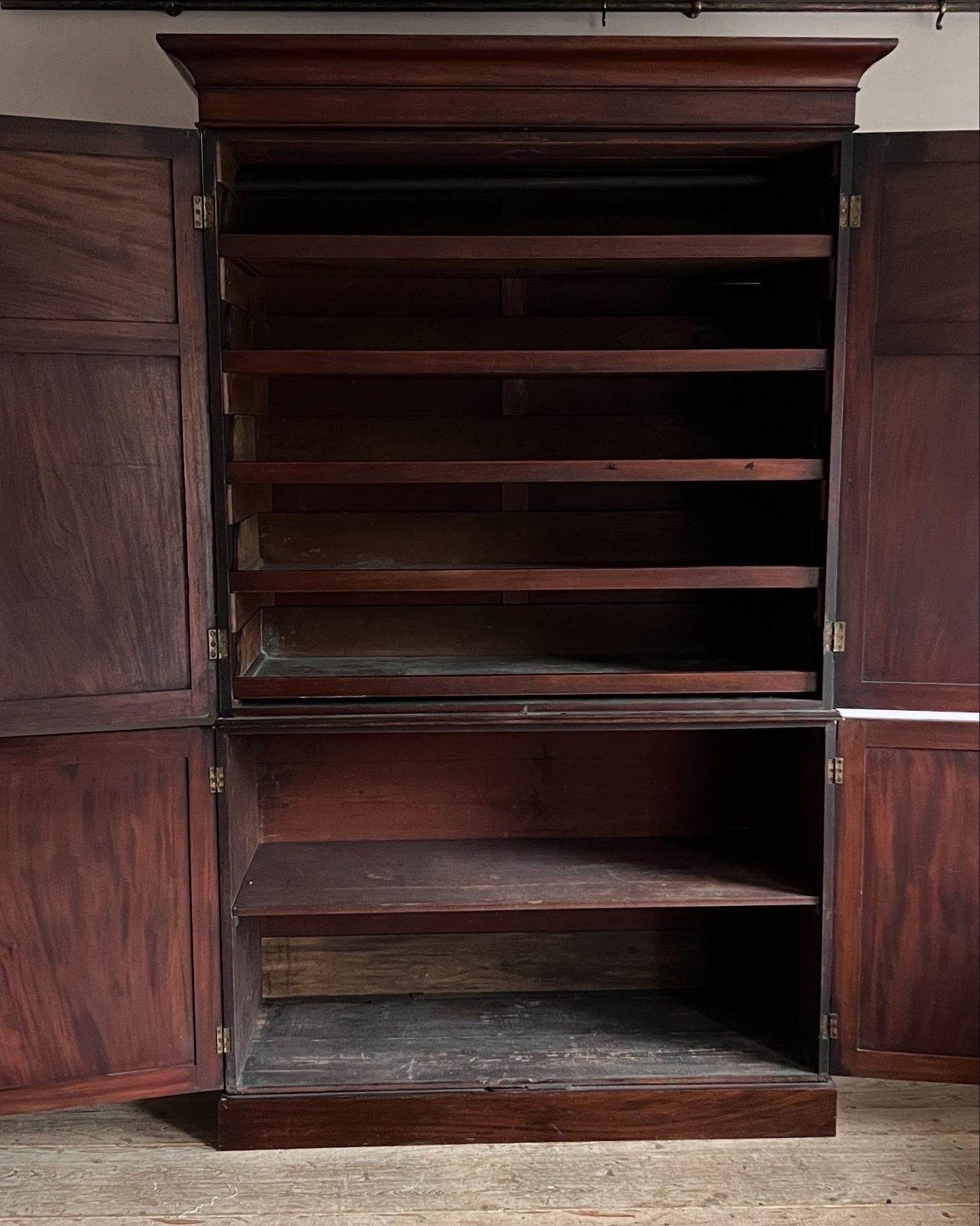A large and handsome mahogany press cupboard, the double doors above hold slides and below is a single shelf. In two parts with a simple cornice, and a plinth base. 
Dimensions; 
H 233cm
W 146cm to cornice (136cm body)
D 56.5cm
