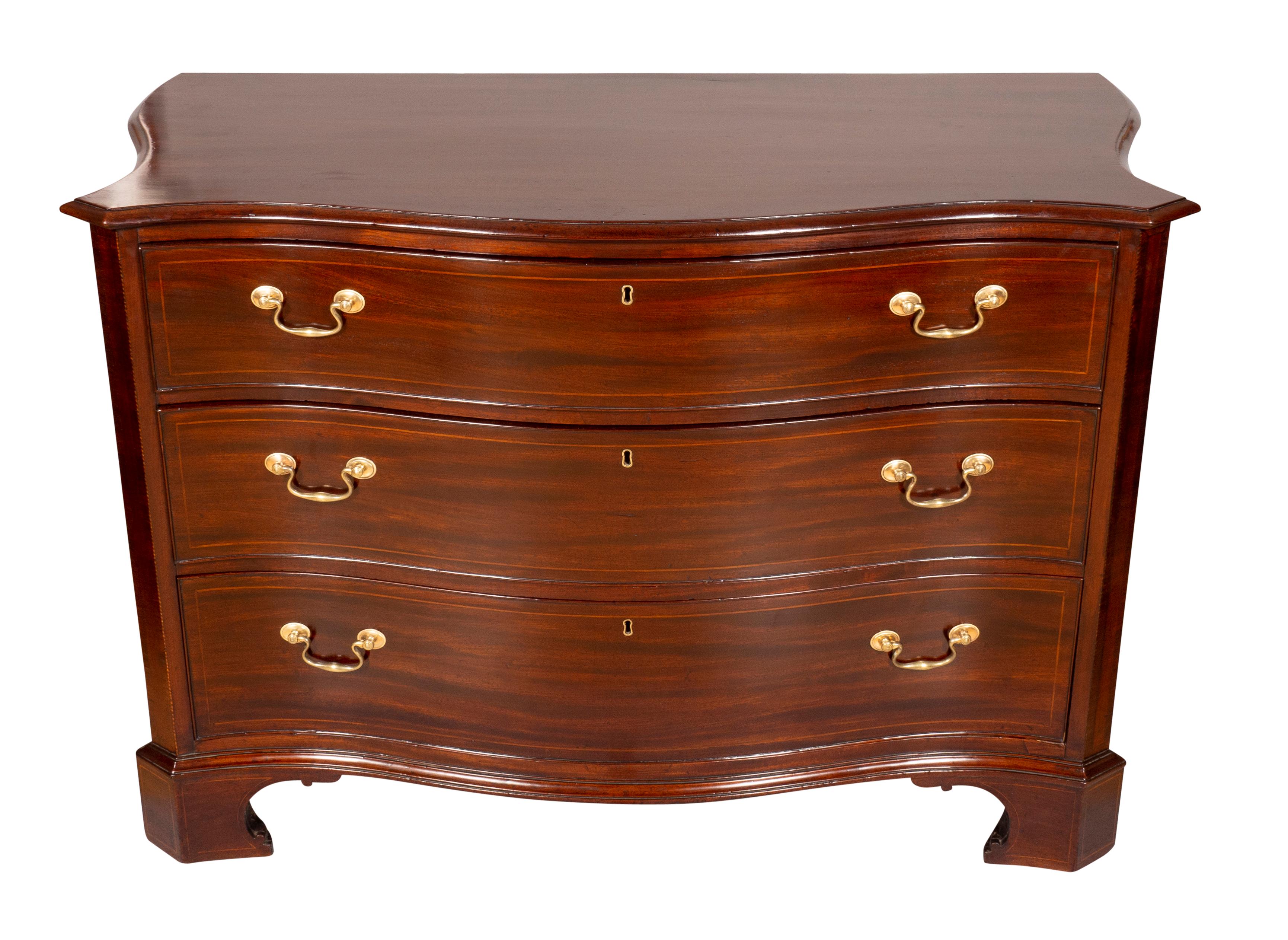 With a serpentine top with shaped edge over three graduated drawers with original brass bail handles flanked by string inlaid chamfered corners, raised on bracket feet. Oak secondary wood. With key.