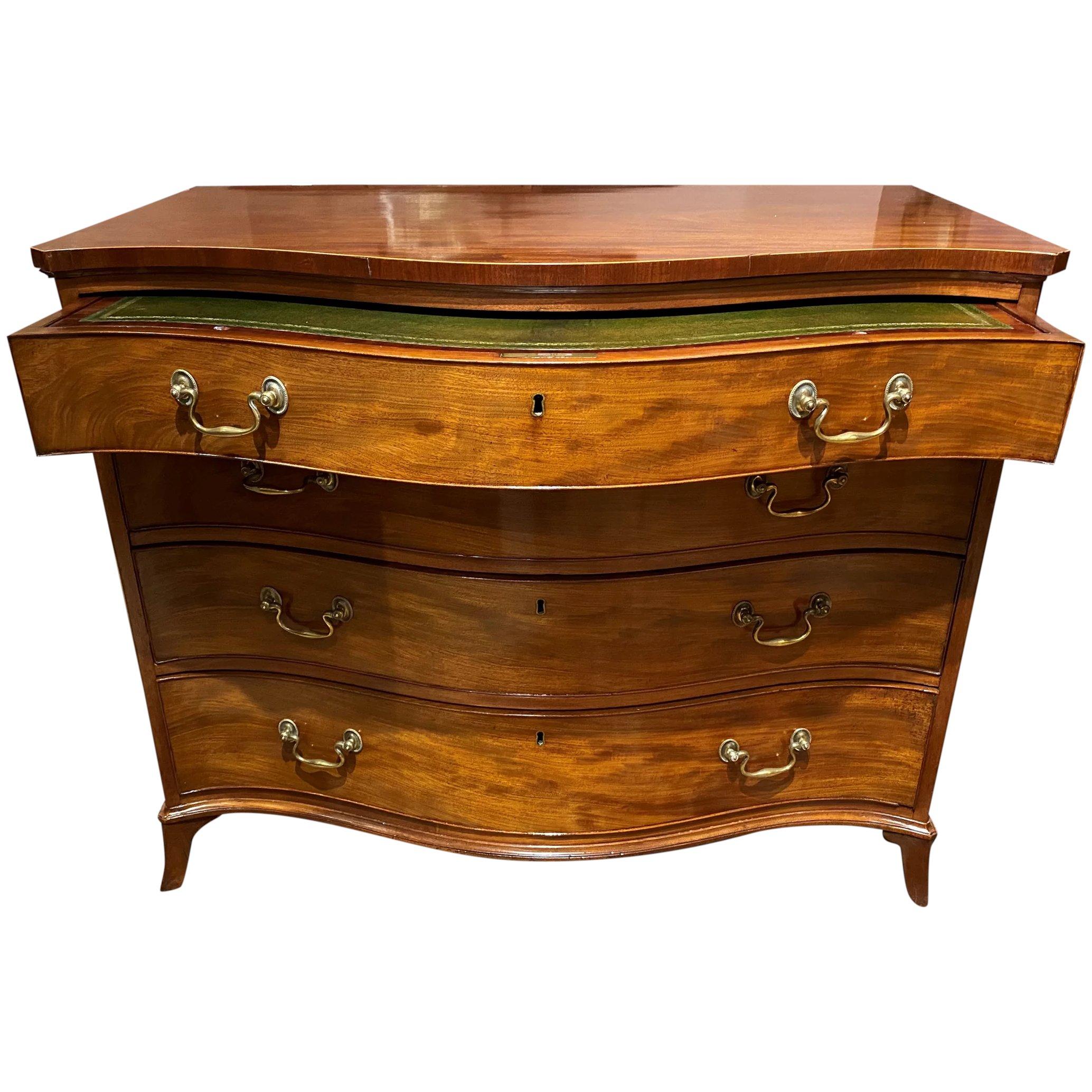 A fine Gillows, George III English mahogany serpentine dressing commode with shaped top surmounting a top drawer with green leather and gold leaf top drawer that pulls out to convert to a desk, enclosing a divided interior with four lidded