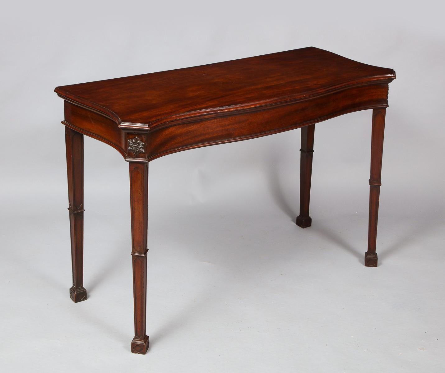 Fine George III mahogany serving or console table having a single board top with rich molded edge and of serpentine form, the canted corners with carved rosettes, standing on blind fretwork tapered legs with Gothic details, having molded collars,