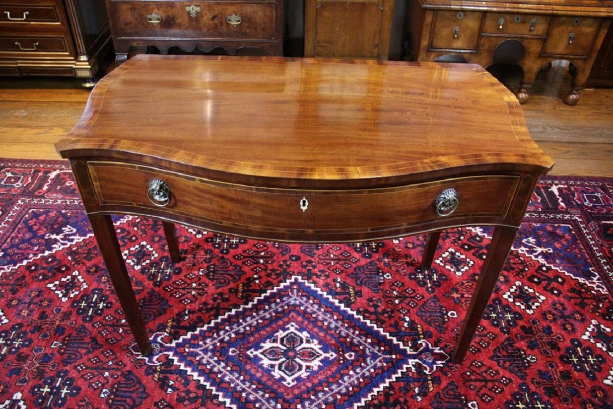 George III mahogany and satinwood crossbanded serpentine side table, possibly Channel Islands. The shaped top sits above a single drawer with table ending in square tapering legs. Boxwood string inlay throughout.