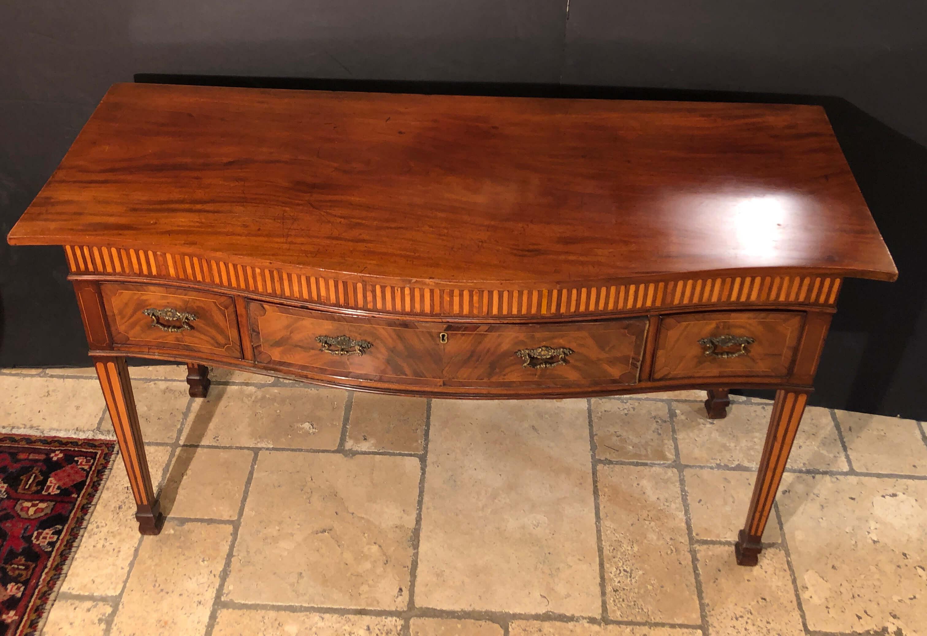 A Rare George III mahogany and satinwood inlaid serpentine sideboard with bookend inlaid frieze, a fitted serving drawer with baize lined top, square tapered bookend inlaid legs and Marlboro feet.
