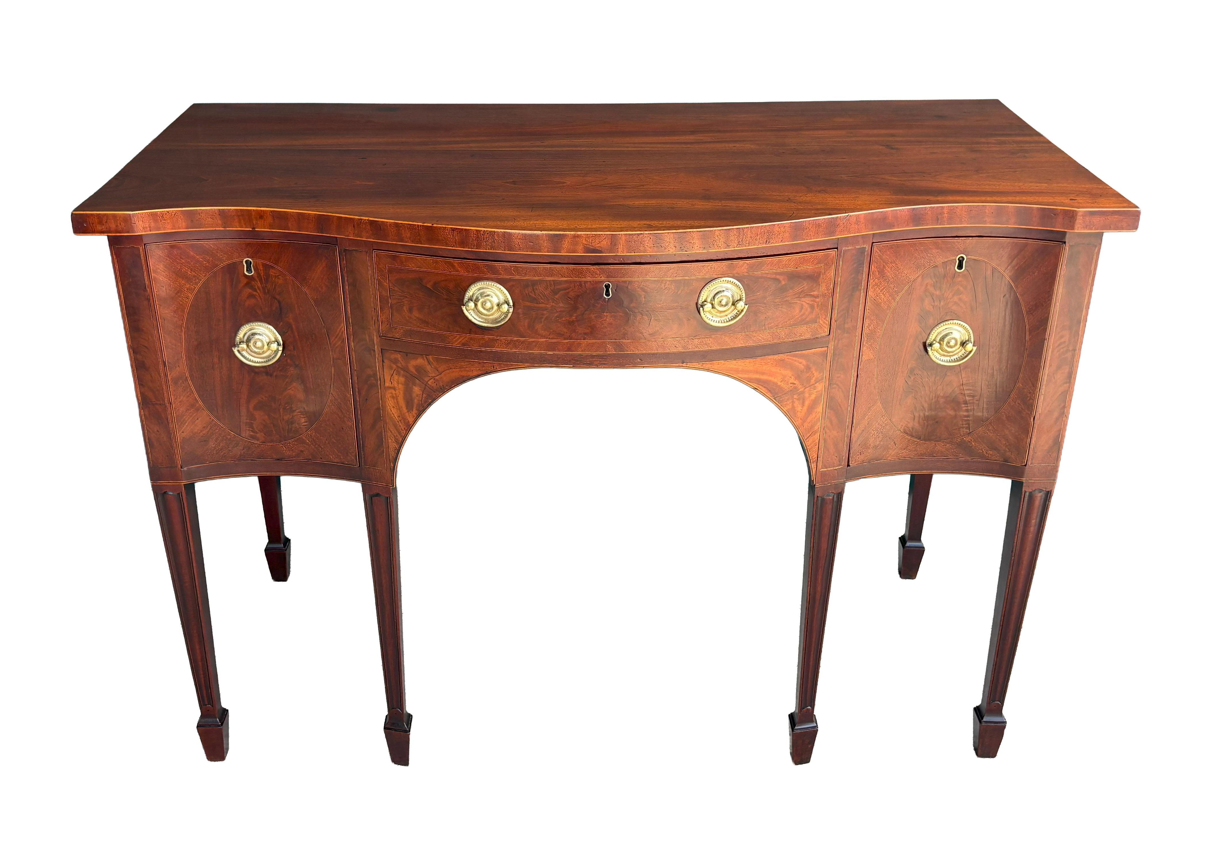 A nice model in great condition. Serpentine top over conforming long cutlery drawer flanked by two deep drawers. Square tapered legs with spade feet. Round brasses