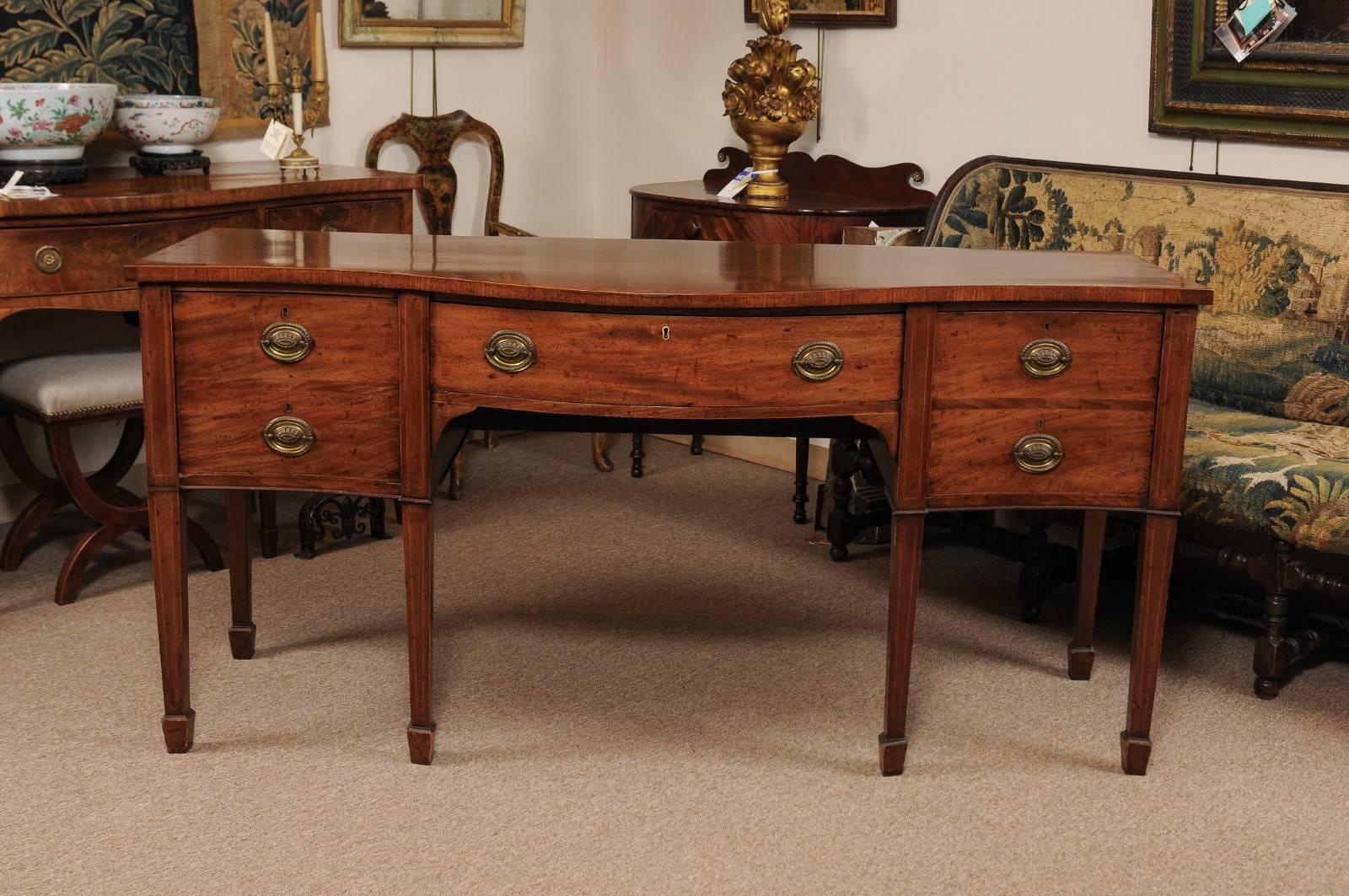 The George III mahogany sideboard with serpentine form, kingswood crossbanding and string boxwood inlay. The frieze with long center drawer and two deep cellarette drawers on opposite sides. All supported by tapered legs terminating in spade