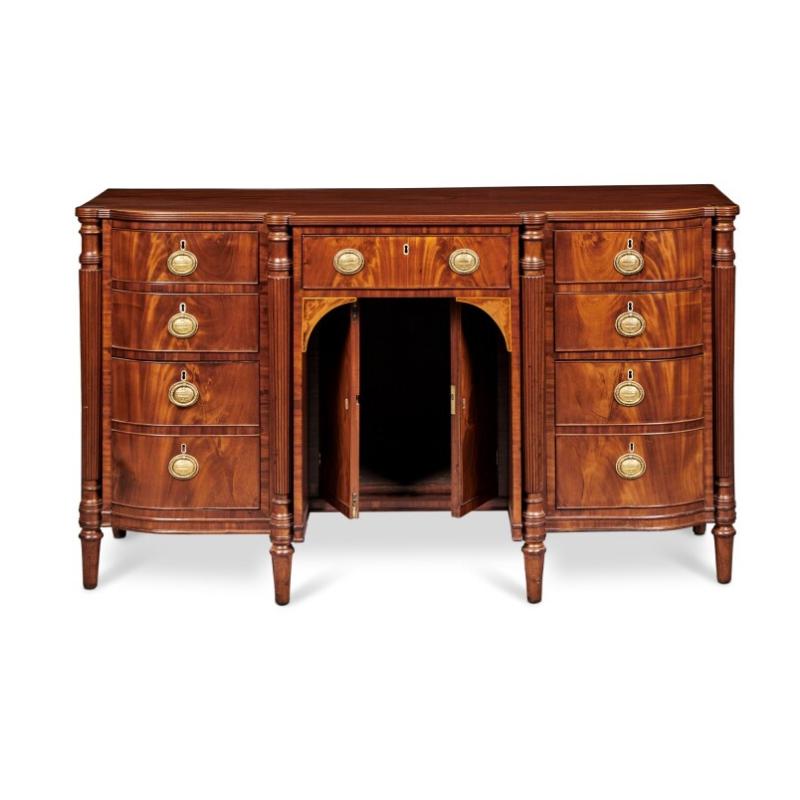 With a rectangular top with bowed front over a central drawer over a niche with a pair of cabinet doors flanked by banks of drawers all flanked by reeded columns and raised on turned tapered feet. Provenance. With Hyde Park Antiques NYC.