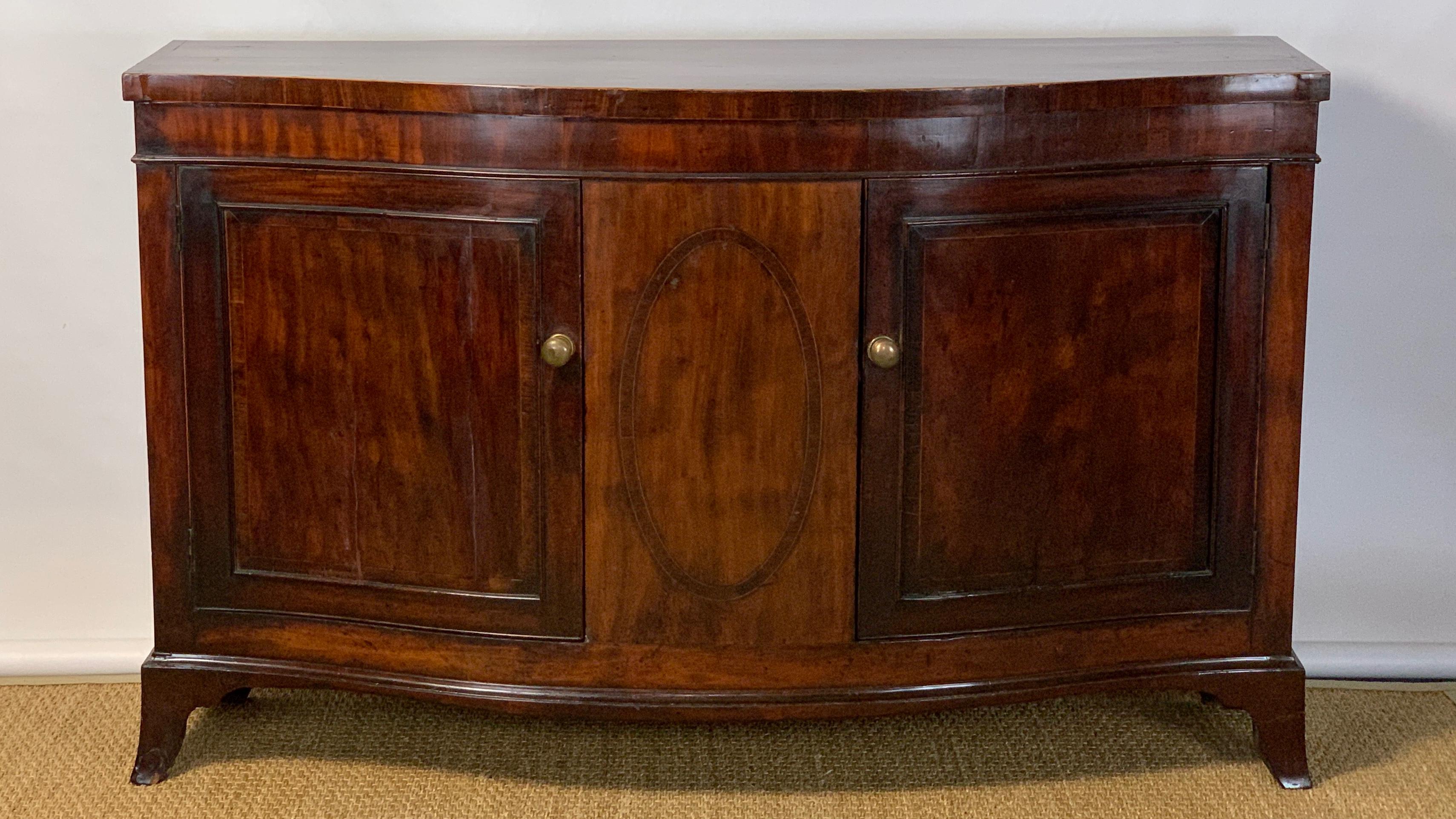 A large and elegant late 18th century mahogany serpentine fronted two door side cabinet or credenza, the interior revealing two large shelves accented with original brass hardware and resting on French splayed feet. The early stamp on the back