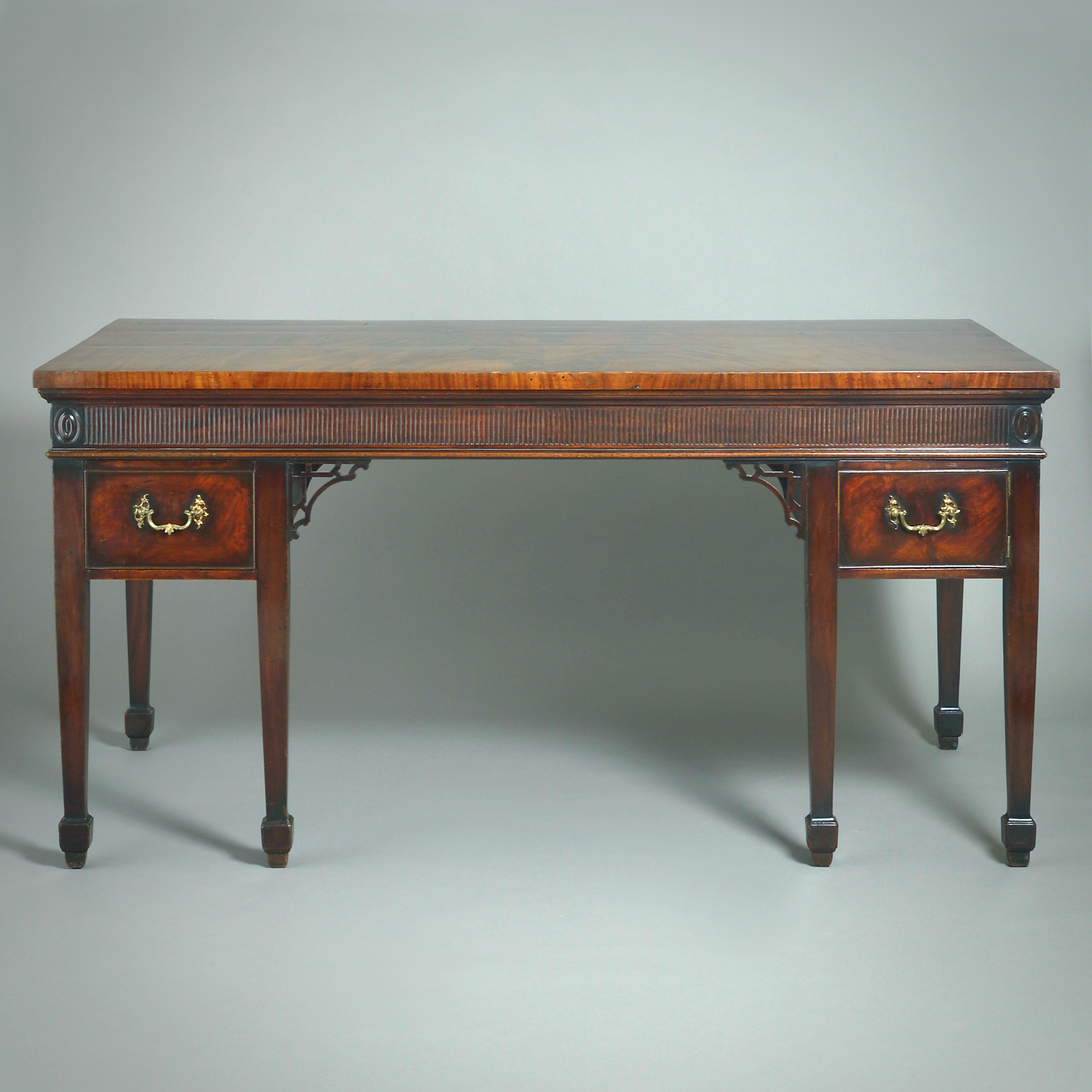 EIN FEINER GEORGE III MAHAGONI-BEISTELLTISCH, ZUGESCHRIEBEN MAYHEW & INCE, UM 1770.

Mit fein strukturierter, buchförmiger Platte über einem kannelierten Fries mit ovalen Medaillons und einer Schublade und Schranktür auf quadratischen, spitz