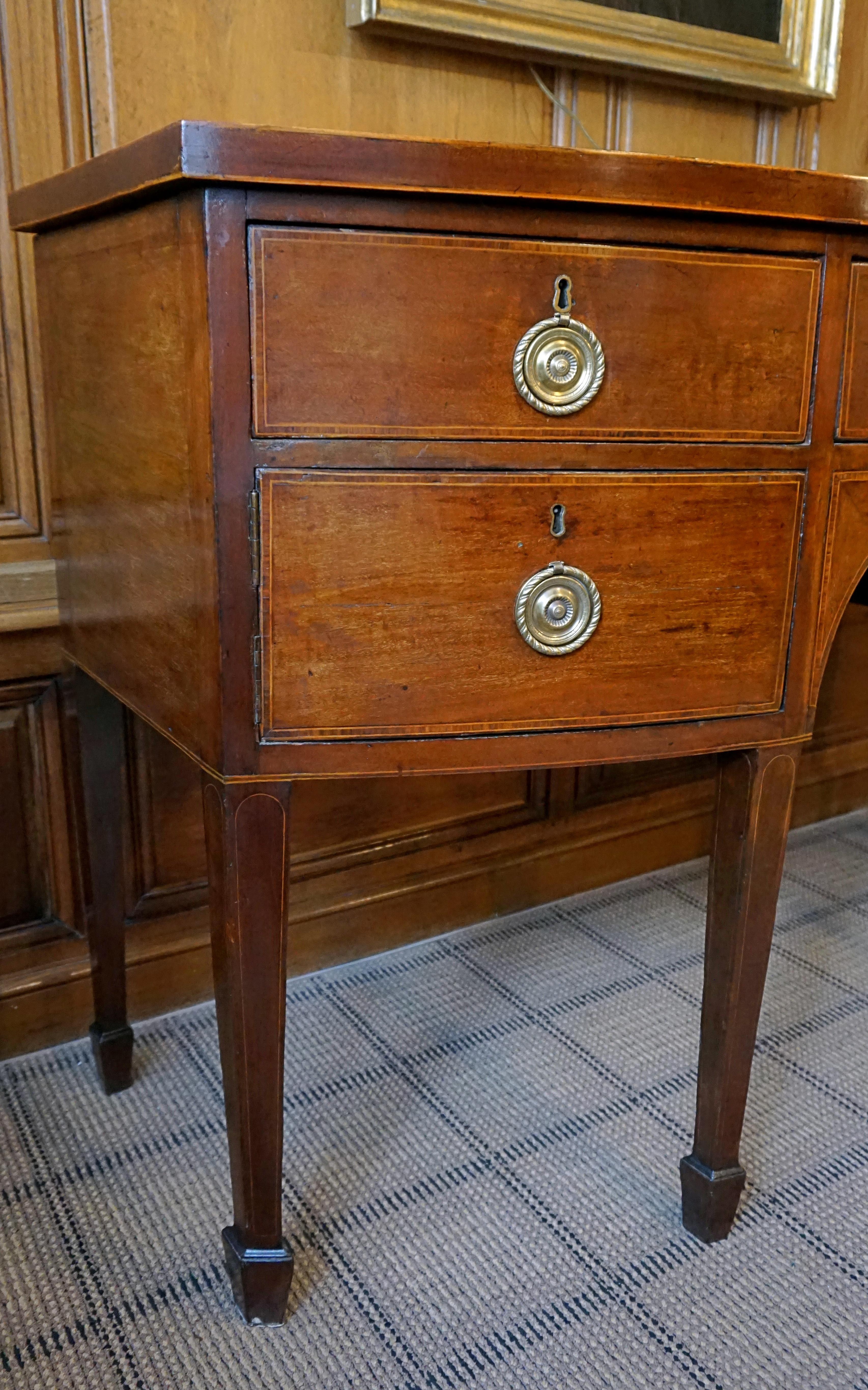T Bow-Fronted top with stringing on edge above three short & two deep cross banded drawers
flanked with an arched niche , raised on square tapering legs 
ending in spade feet With brass handles & hardware 