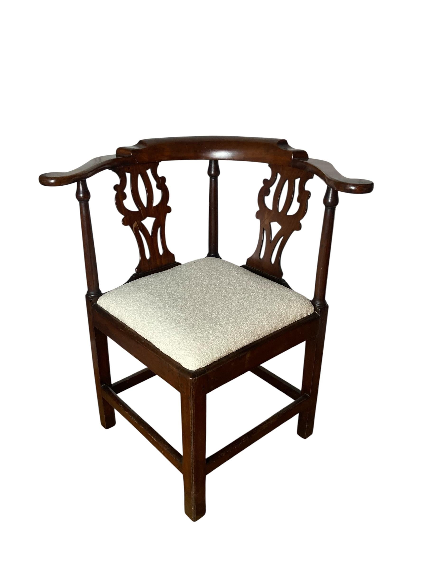 Sedia angolare ad arco in mogano di George III con ringhiera a volute, stecche sagomate e traforate sopra un sedile impagliato, sollevata su gambe quadrate smussate unite da barelle. Caratterizzata da una morbida seduta imbottita in bianco in stile
