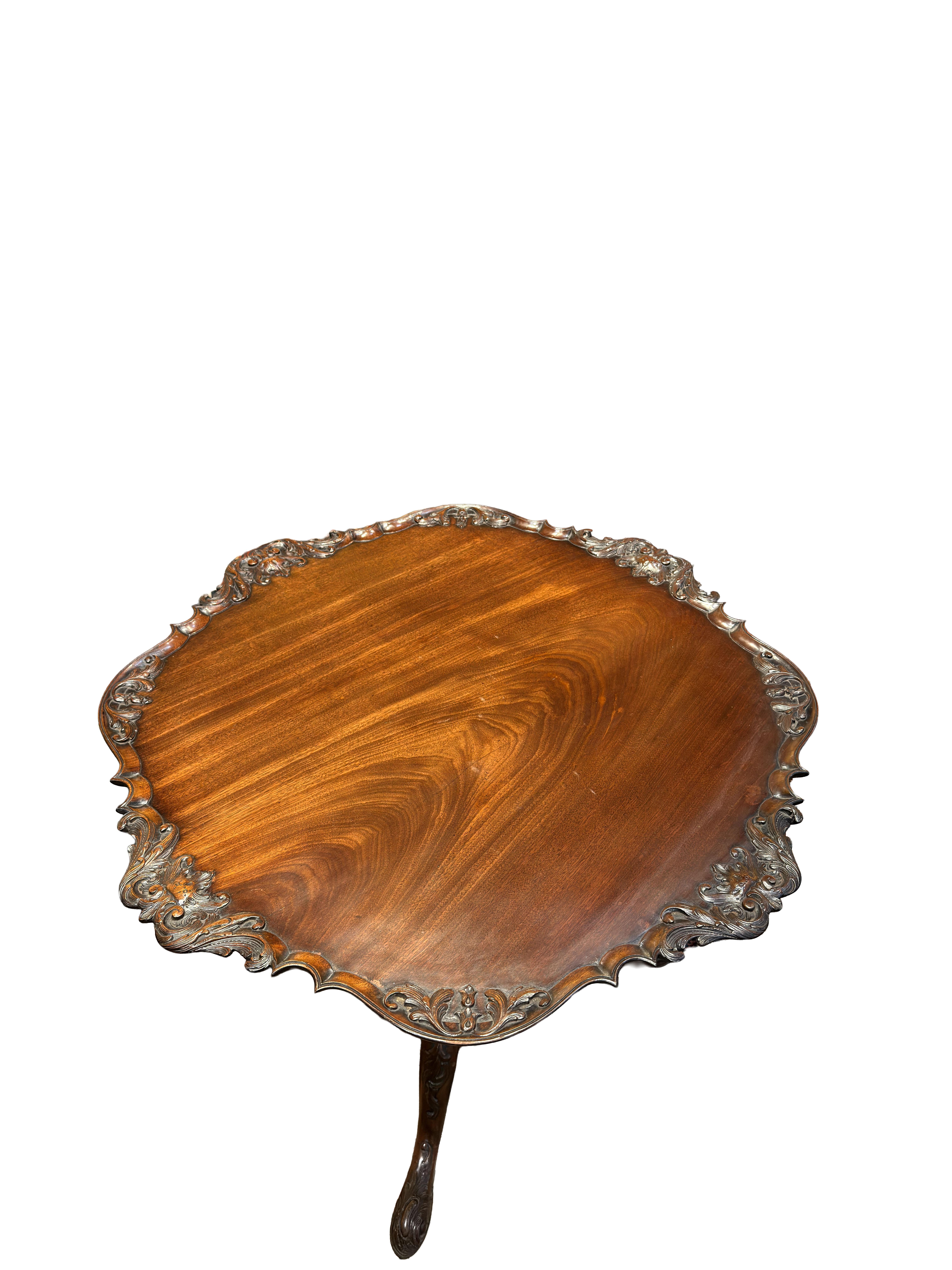 An exceptional George III mahogany tea table which features a single board top adorned with intricate foliate carvings encircling its outer edge. A reeded and carved column stands prominently, culminating in cabriole legs that terminate in