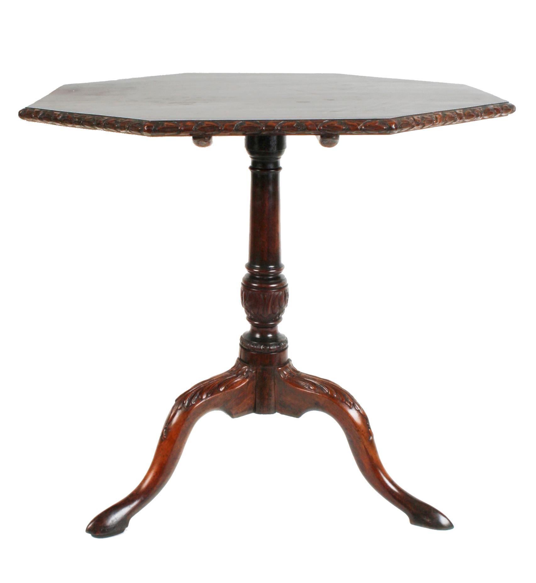 George III mahogany tilt top table with a ribbon and leaf carved edge, raised on a carved and turned center post, with three out-swept cabriole legs with acanthus leaf carved knees. It has a brass sliding latch lock mechanism that keeps the table