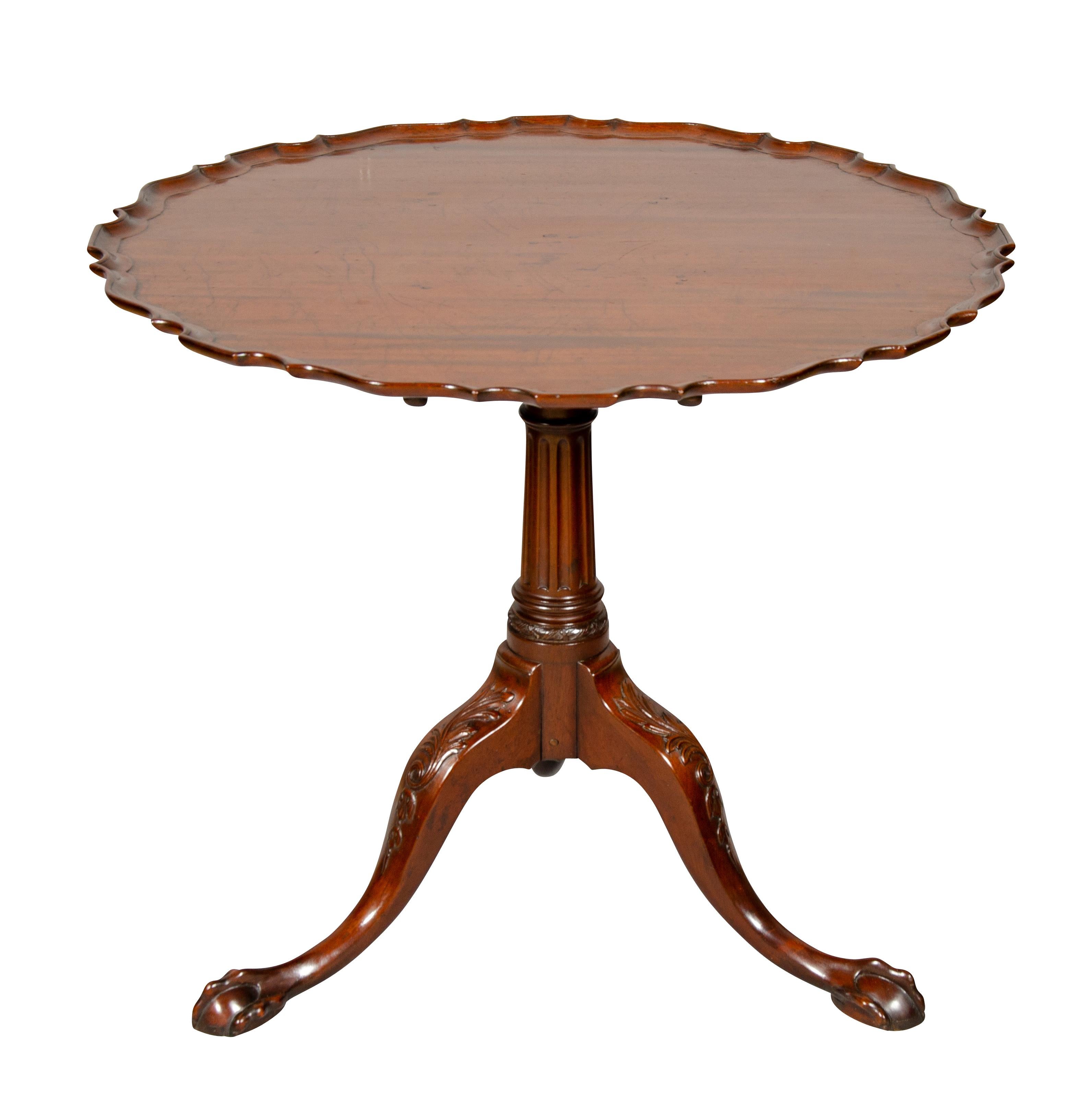 With circular hinged pie crust top on a cylindrical fluted support joining three cabriole legs with knees carved with scroll leaf ending on claw and ball feet.