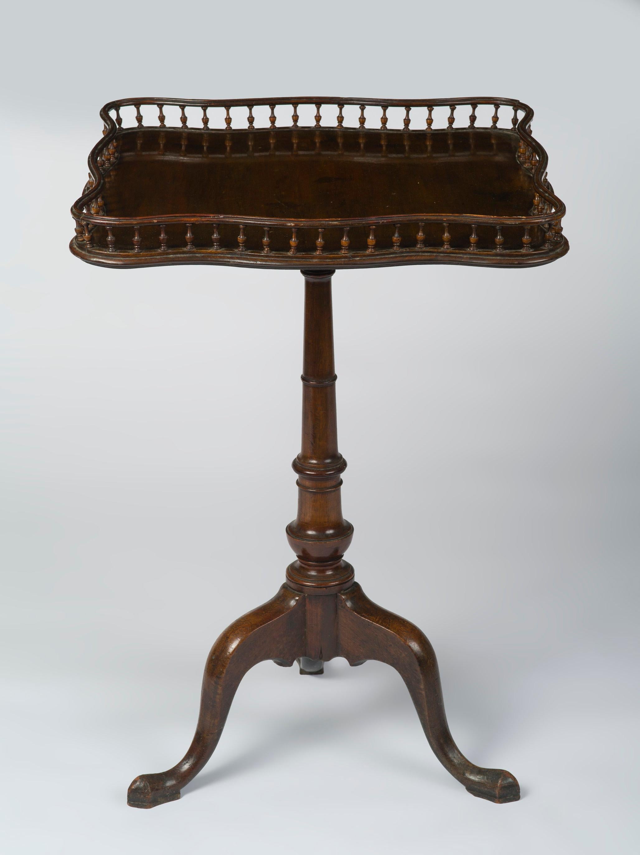 The square serpentine tilt-top with a spindle gallery, above a tapering turned column raised on three cabriole legs terminating in pad feet.
   