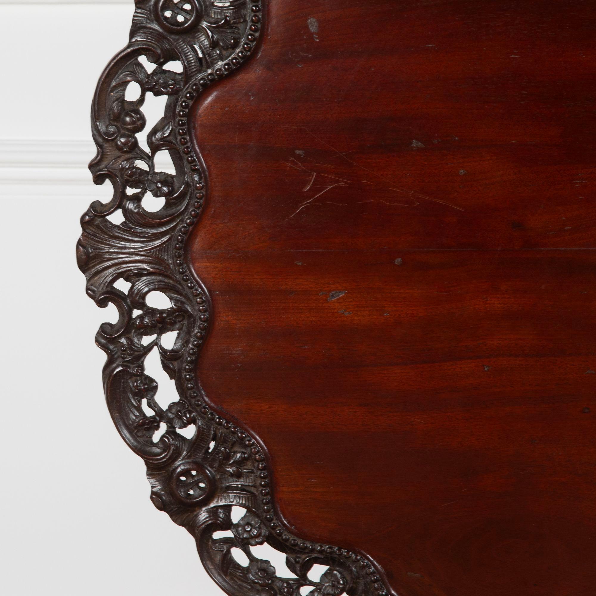 Dreibeiniger Tisch aus Mahagoni George III.
Die runde Platte mit einem geschnitzten, durchbrochenen Rand auf einem fein geschnitzten, mit Blättern besetzten Baluster als zentrale Stütze hat mit Akanthusblättern besetzte Schneckenbeine, die in