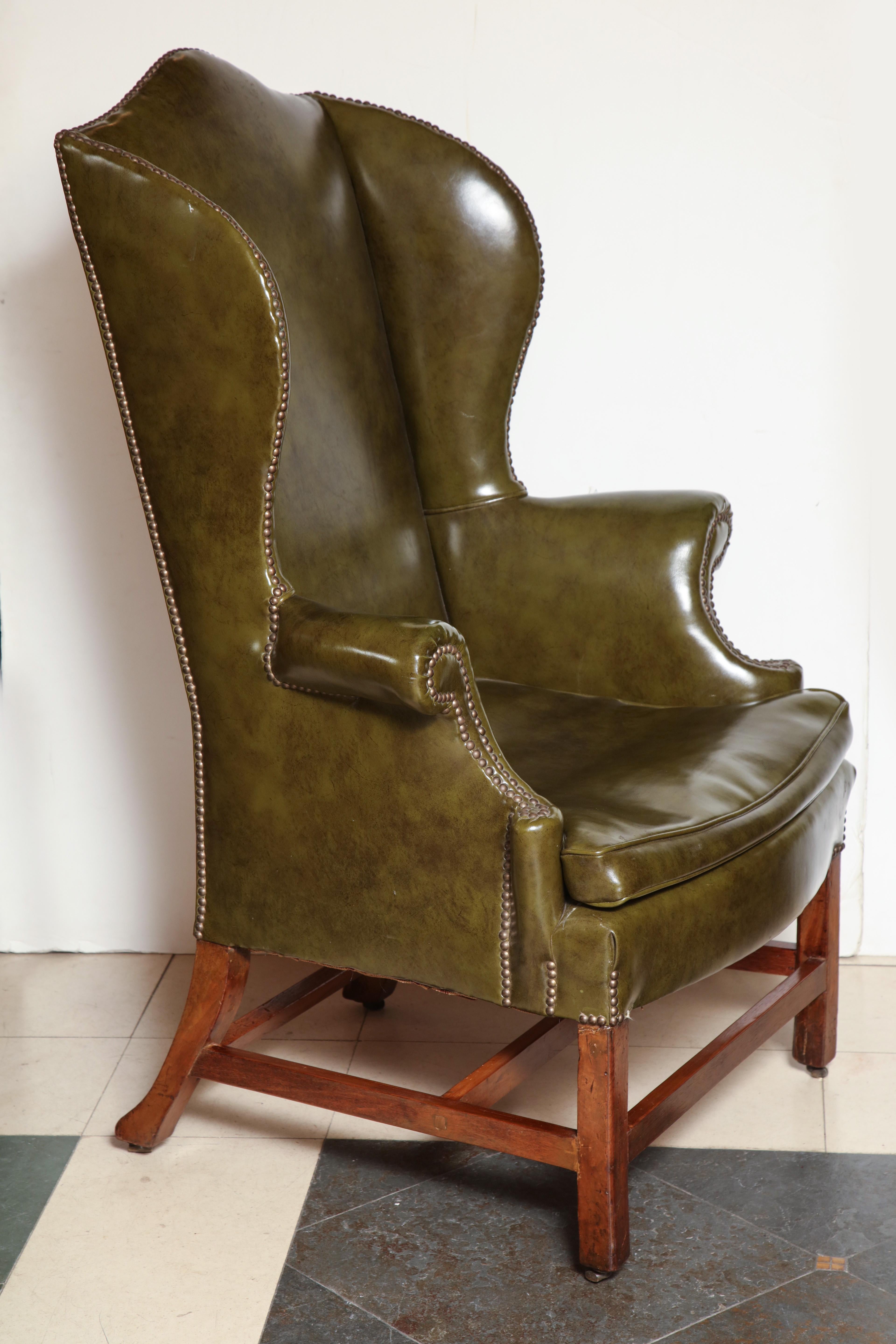 A fine English George III mahogany leather upholstered high back wing chair with scrolling arms and a stretcher base.