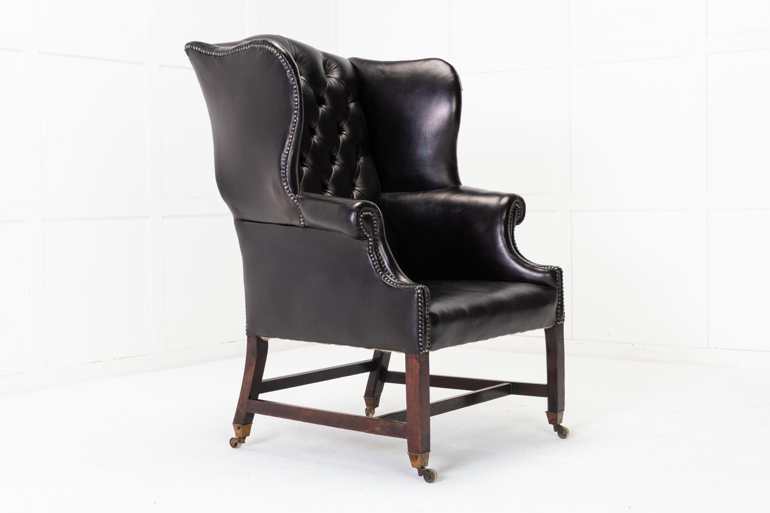 A good sized, shapely and well proportioned George III, English 18th century, mahogany wing chair.

Upholstered in black leather having a tall buttoned back and generous rolled arms and studded detail. Supported on mahogany legs with traditional