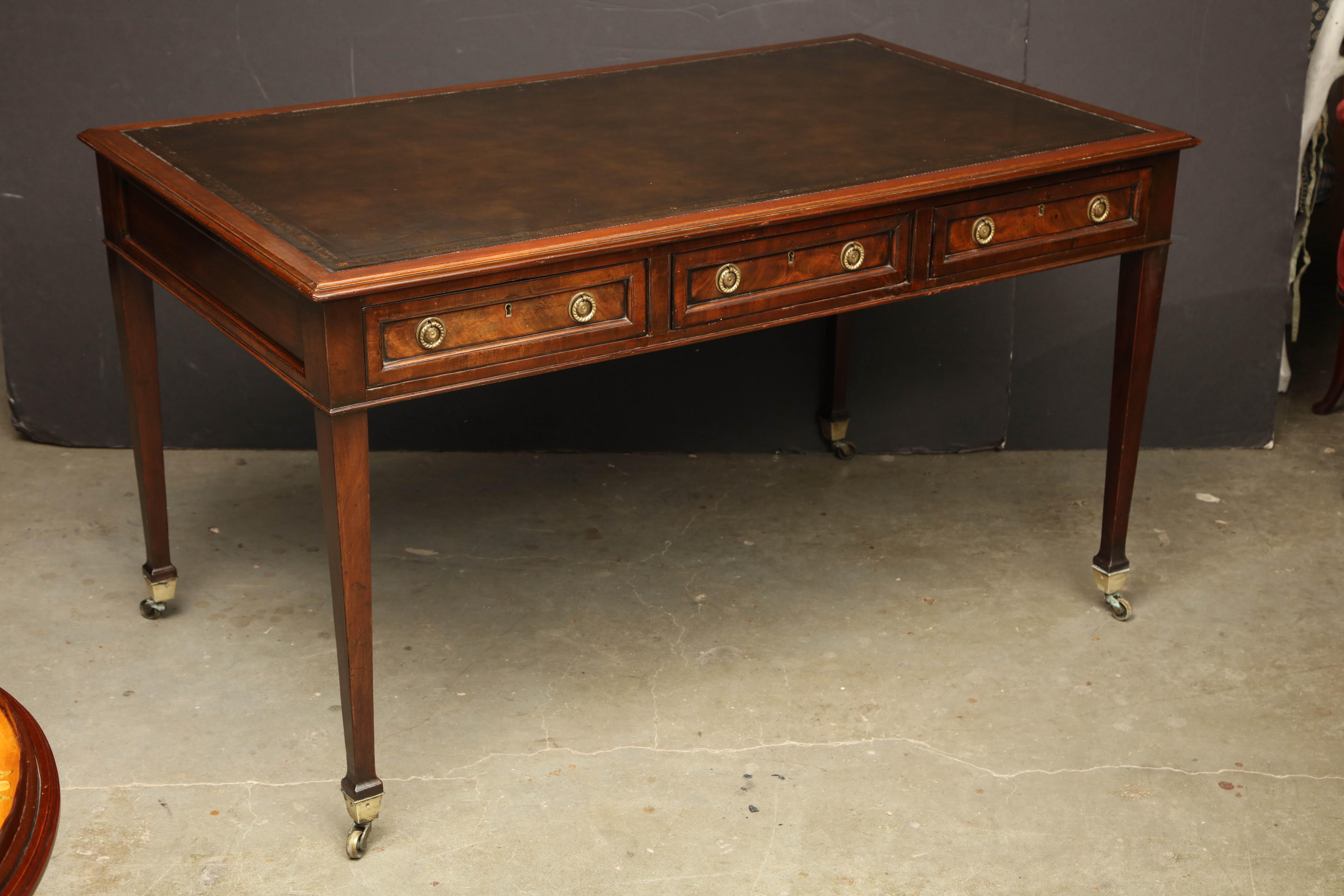 A fine George III leather top mahogany writing table with three drawers, molded edges, a tooled border leather top on square tapered legs with brass caster feet.