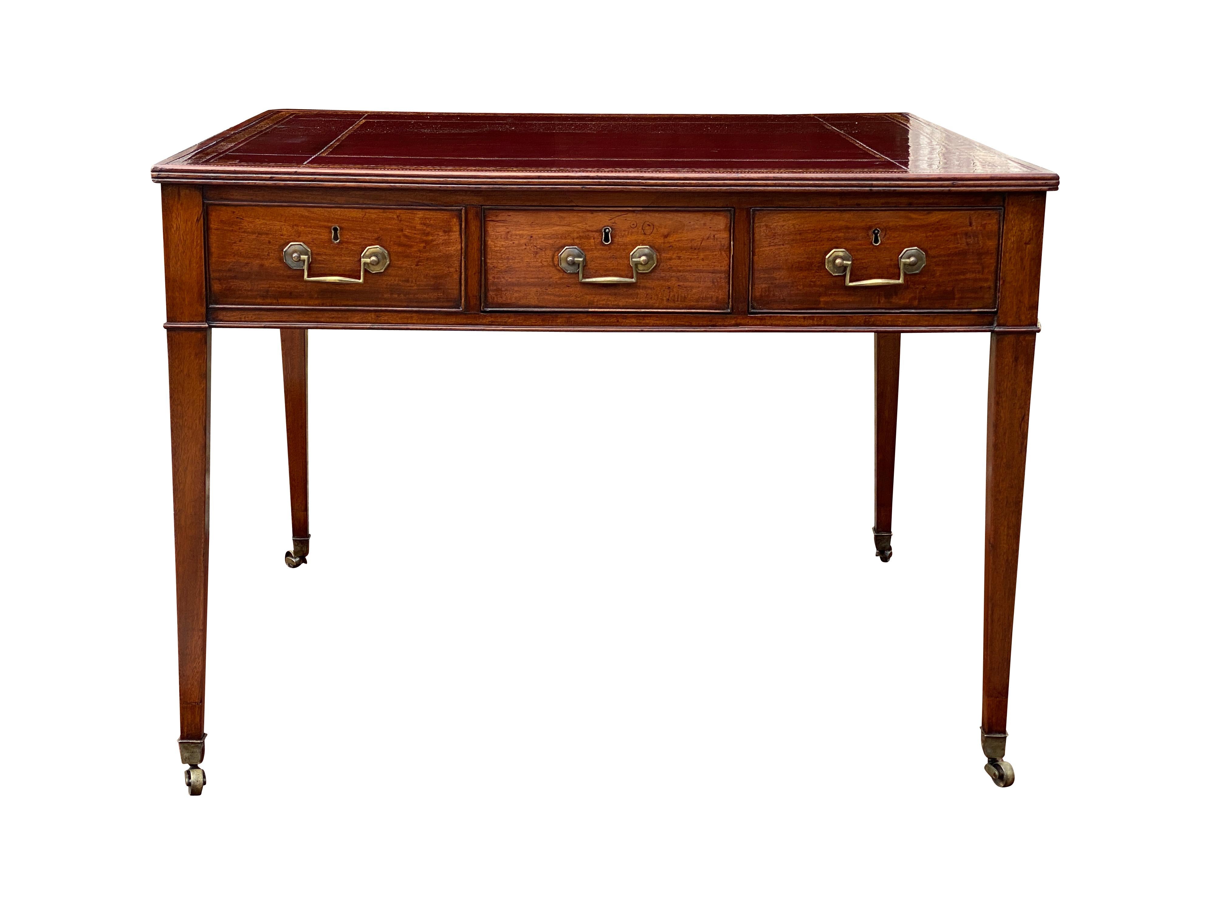Rectangular top with inset deep burgundy leather with some flaws over three drawers with one central drawer on the reverse flanked by two false drawers, raised on square tapered legs and casters. Square brass bail handles.