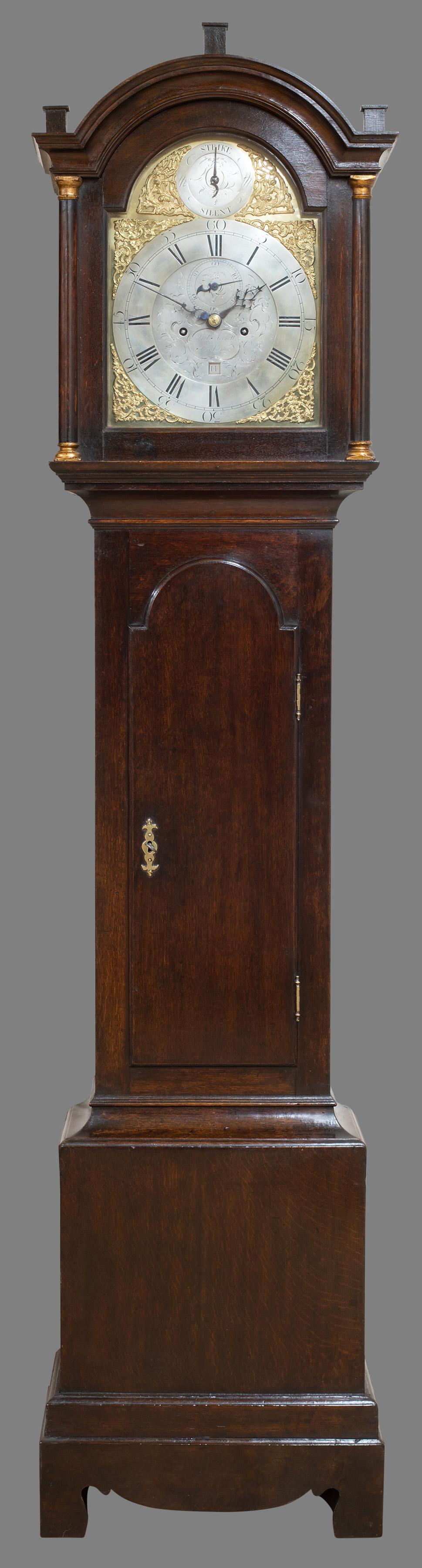 George III longcase clock

George III oak longcase clock standing on a double stepped base with long trunk door and brass escutcheon. Integral hood pillars with brass capitals supporting the glazed hood door surmounted by a break arch pediment