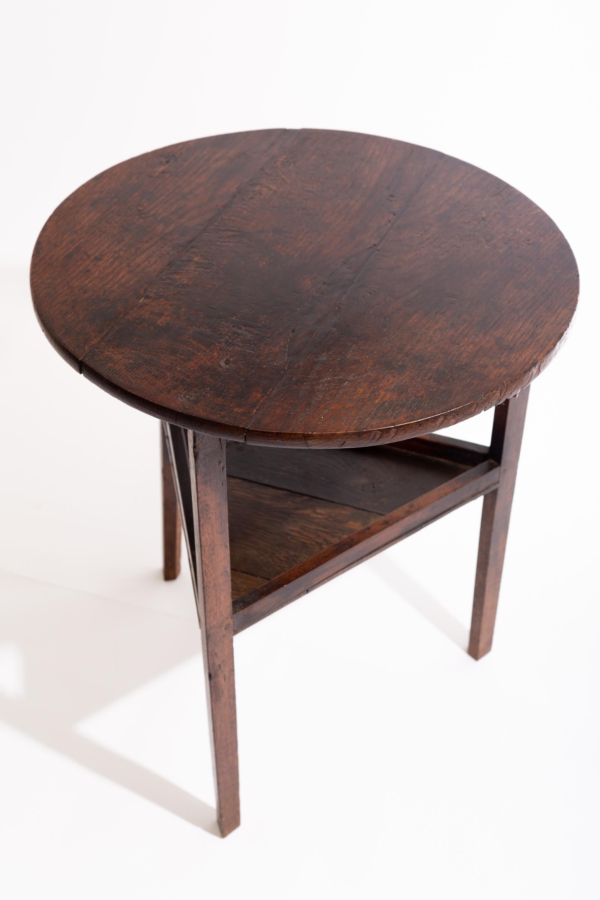 Table de grillon en chêne de George III avec un plateau circulaire au-dessus d'une base triforme avec des pieds effilés reliés par une étagère surélevée.

Construction solide et riche patine d'usage. Porte les coups et les fissures typiques de l'âge
