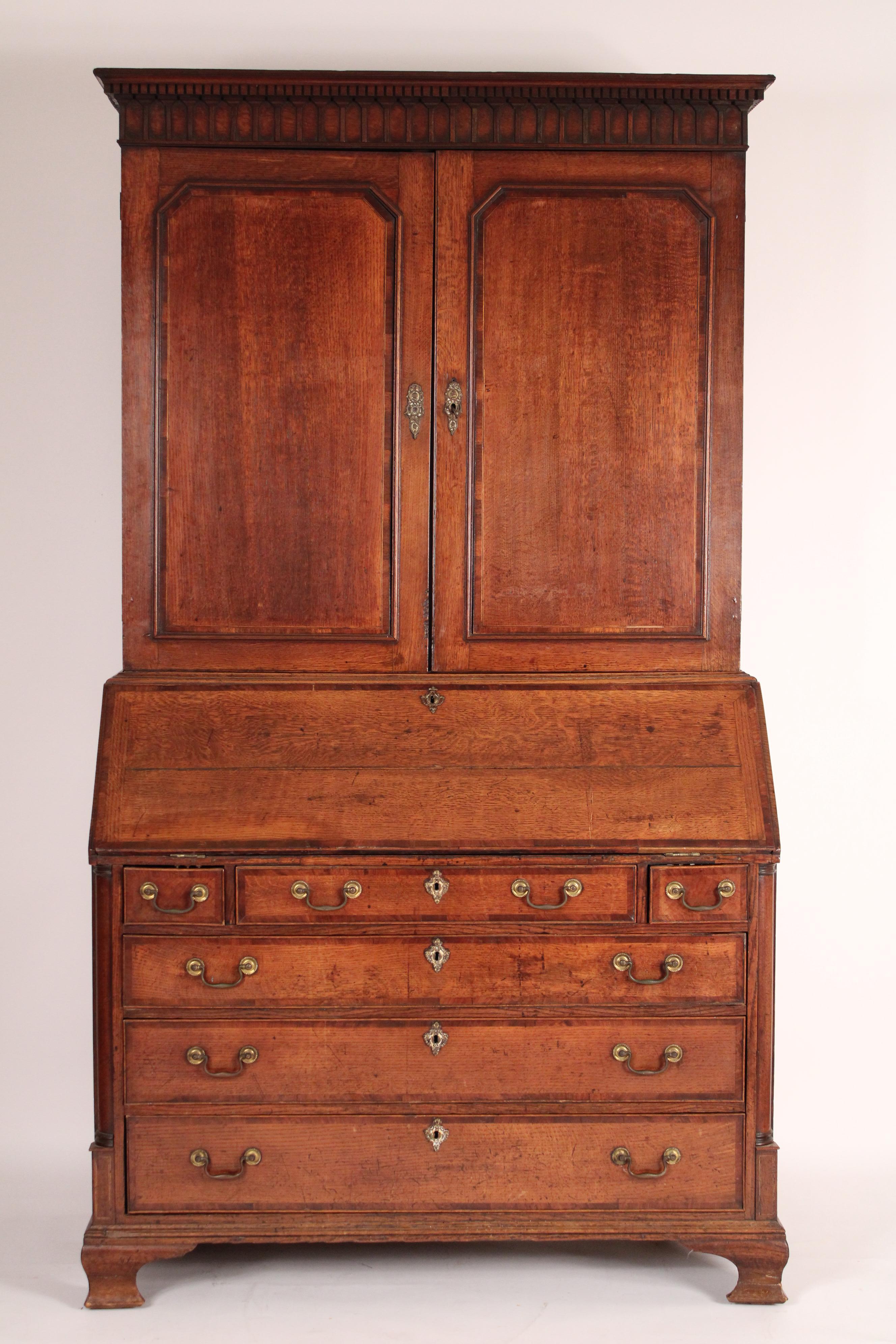 George III quarter sawn oak secretary, circa 1810. With a concave cornice, dental molding, two quarter sawn oak doors with mahogany crossbanding, a quarter sawn oak slant top with mahogany crossbanding, the interior with a central prospect door with