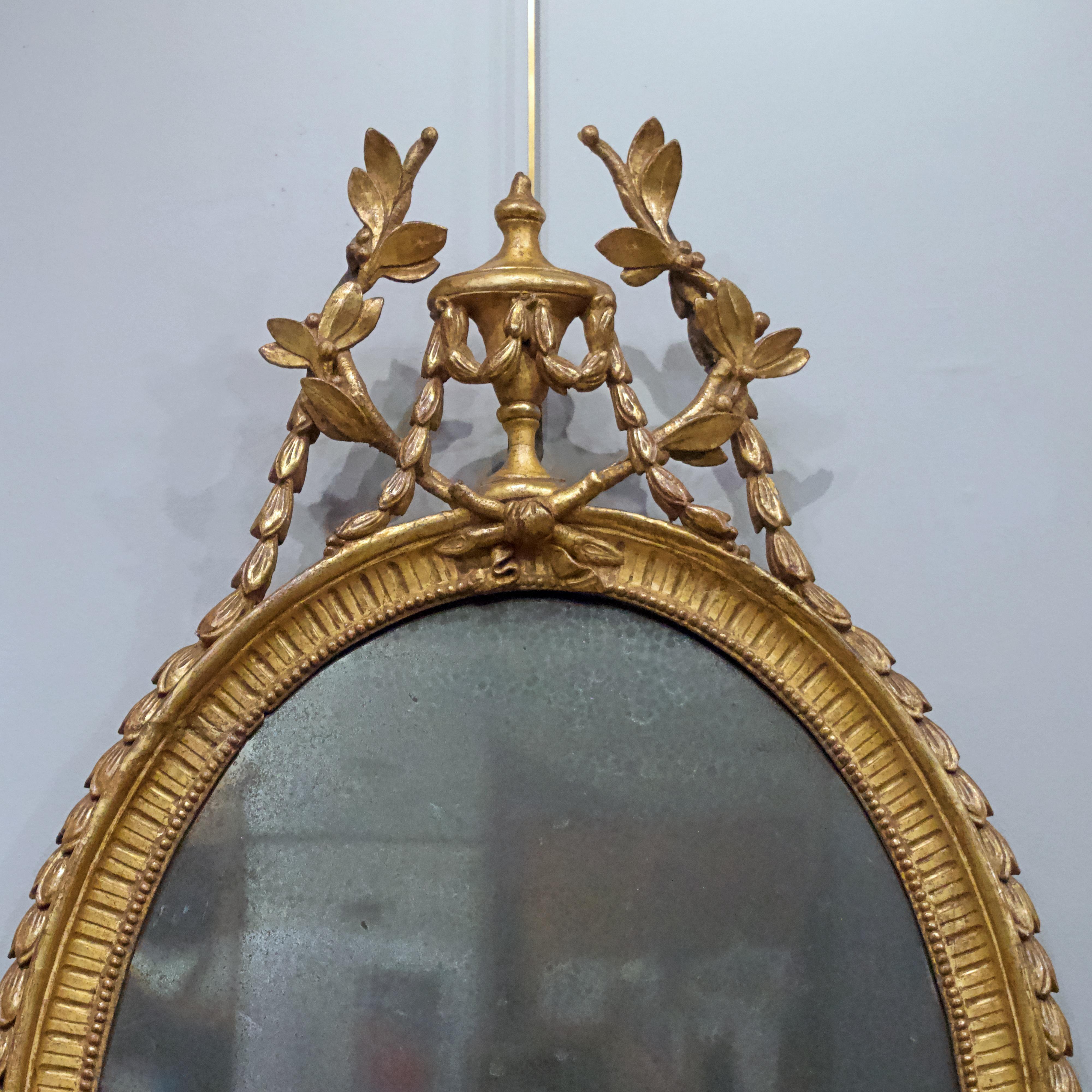 A George III oval giltwood mirror, late 18th century
 
The urn shaped finial centered on foliate swags
the oval frame with carved detail, over a central
Rosette patera, flanked with floral decoration.
With original mirror plate, heavily but
