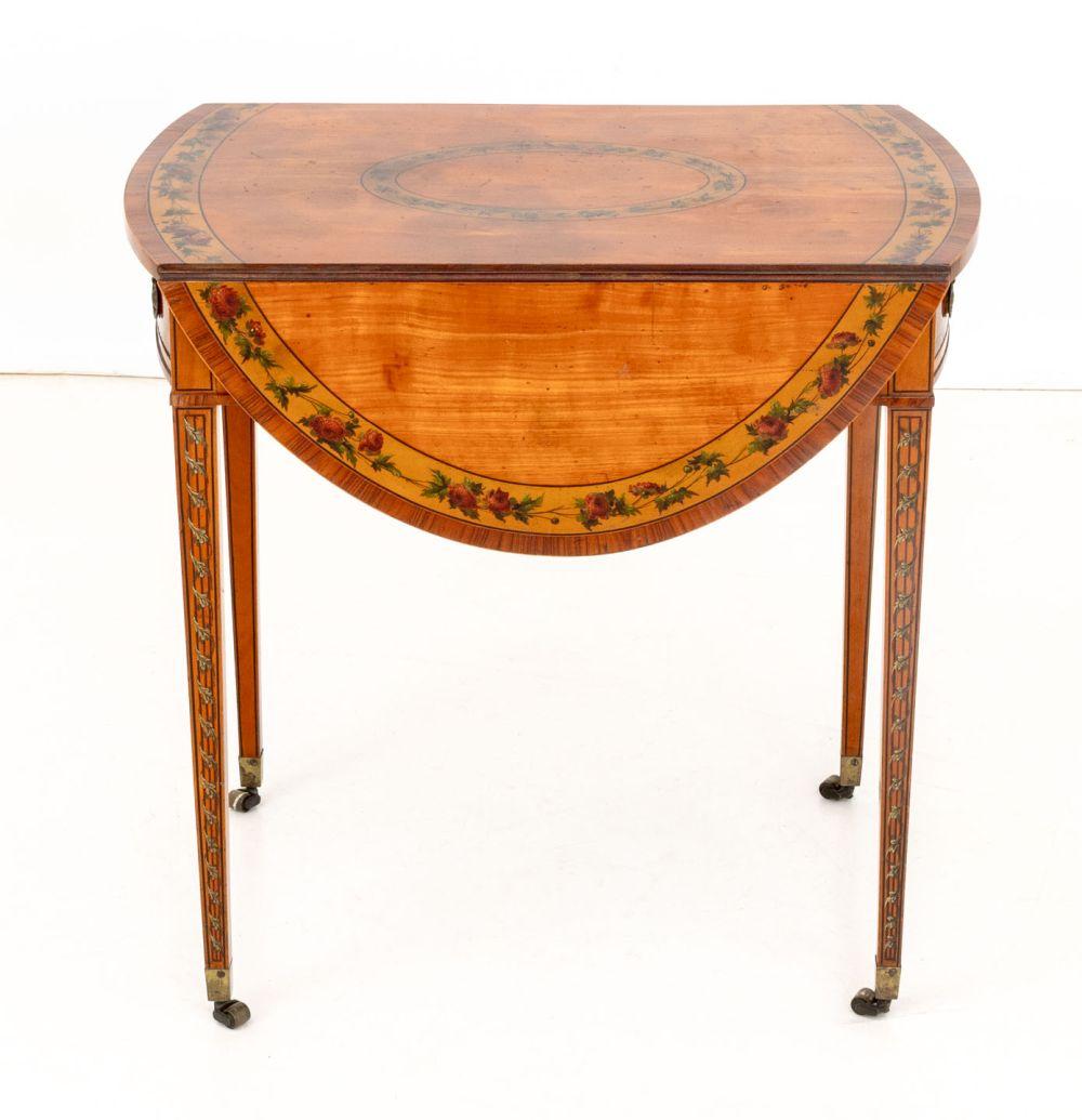 Table Pembroke en bois satiné peint de George III, les côtés tombants s'ouvrant sur un plateau ovale avec une bordure florale au-dessus d'un tiroir avec deux poignées en laiton et un faux tiroir sur l'autre côté, sur quatre pieds fuselés avec