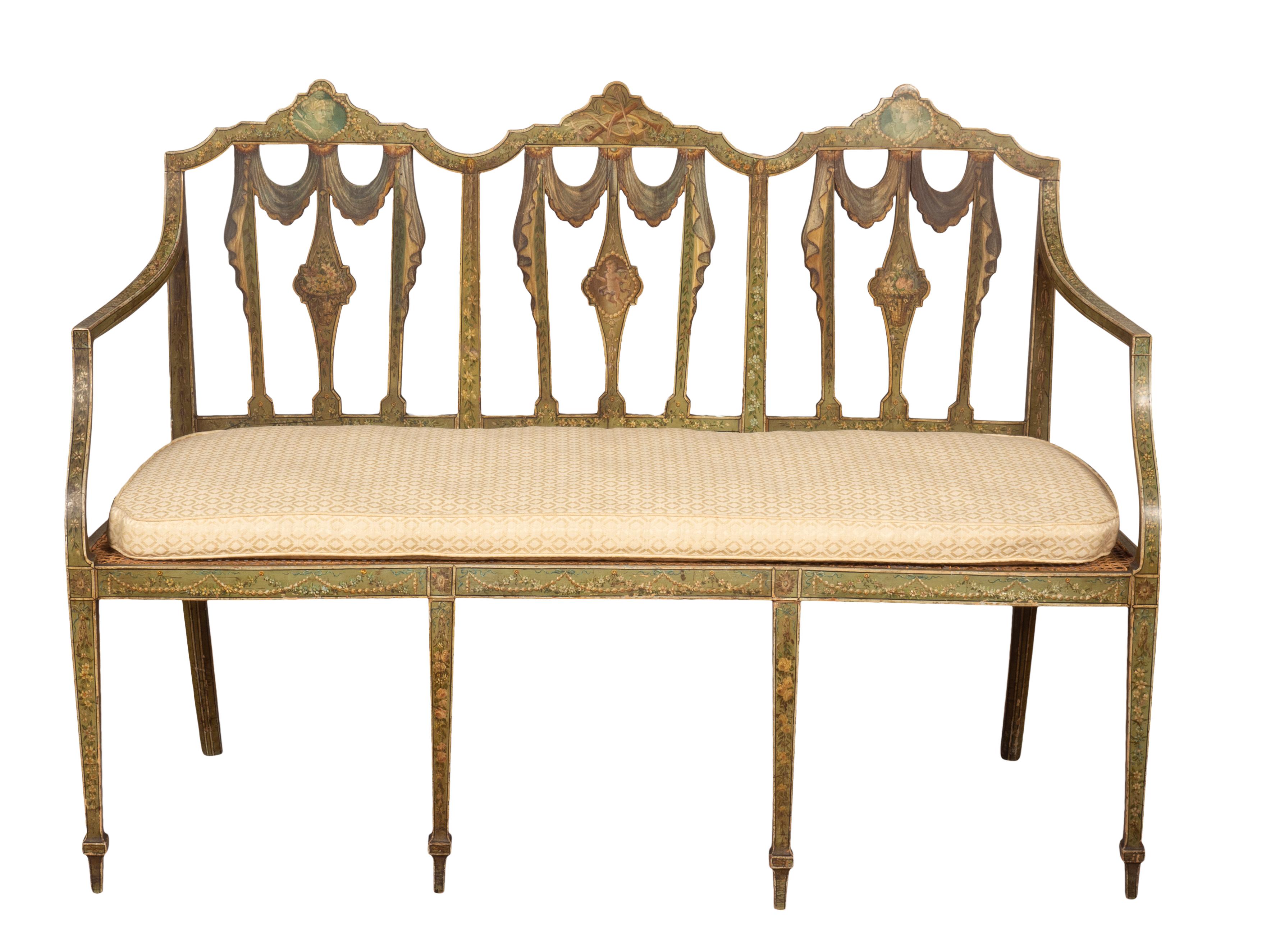 Three chair back with arms and caned seat raised on square tapered legs. the back splats with painted drapery design also musical trophies