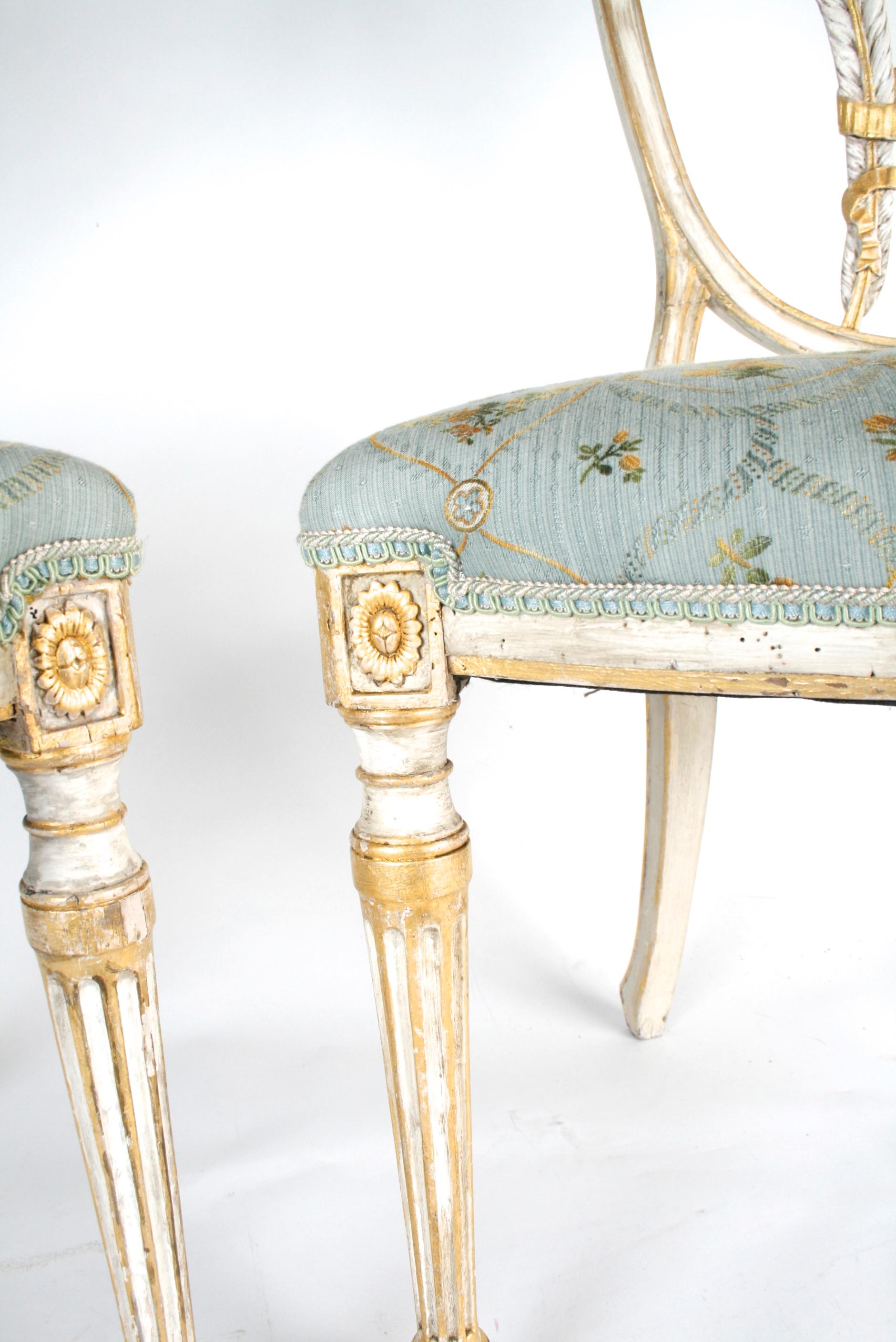 A pair of George III parcel-gilt and painted side chairs with curved shield backs inset with the Prince of Wales feather plumes. The chairs have upholstered serpentine seats that stand on turned and fluted front legs with rosettes. Their seat height