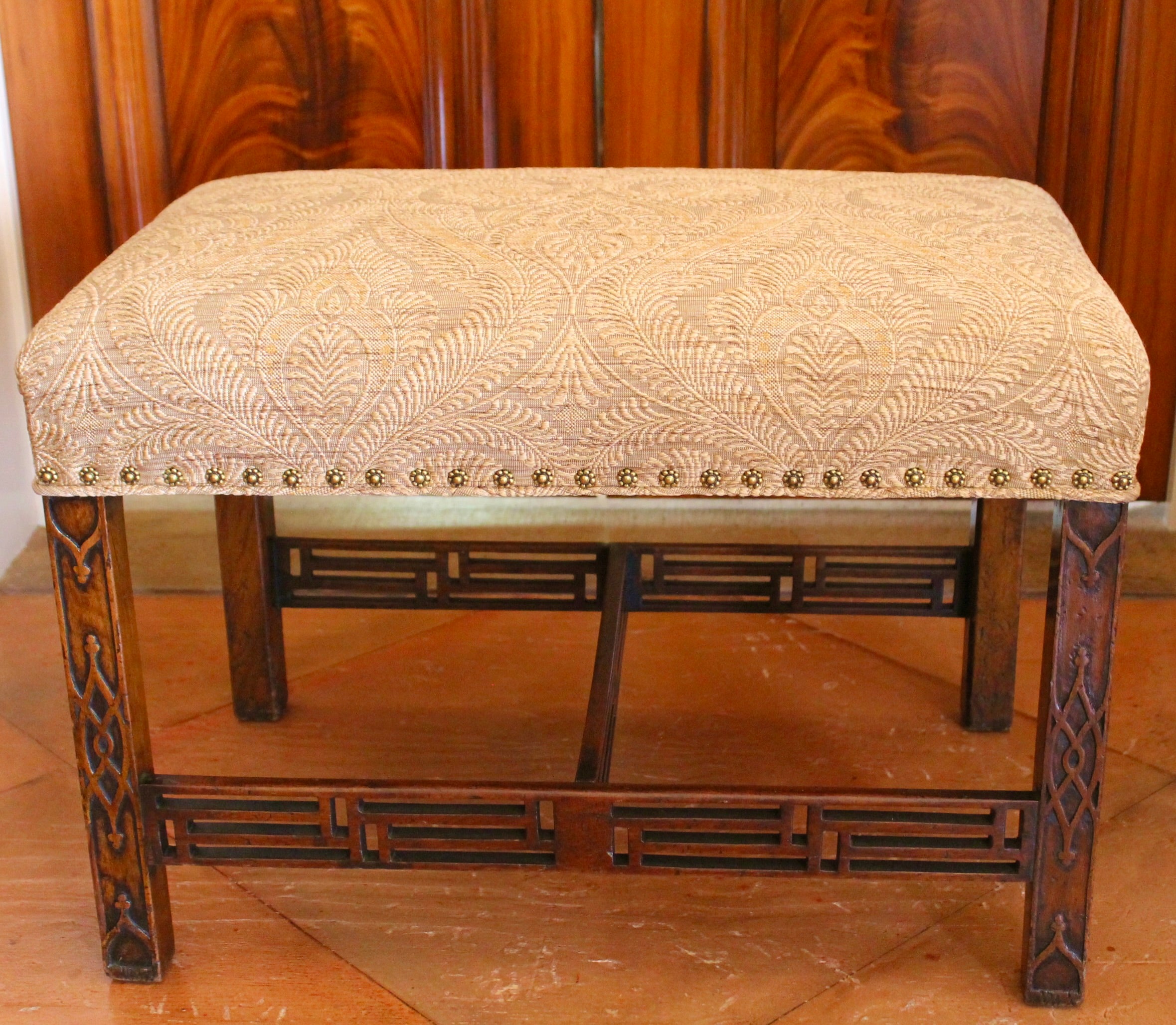 A very good English mahogany bench with blind fret carved legs connected by unusually complex open fret Chinese Chippendale fret stretchers. Freshly upholstered in a chic caramel tan woven fabric and further embellished with brass rosette form