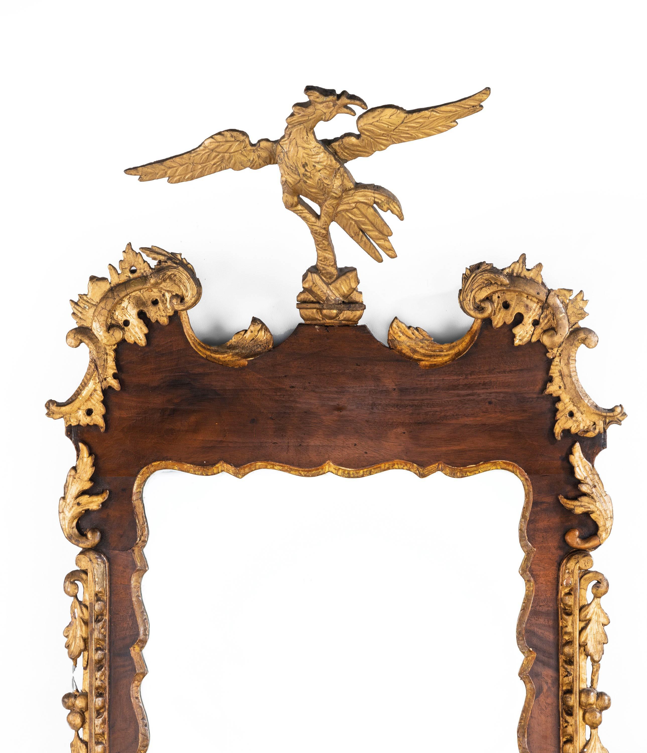 A George II period, very elaborate, mahogany and parcel gilt mirror. The outer frame continuously carved in applied fruits, leaves and foliage. The top surmounted by a flying eagle. The gilding restored at some point during the 19th century and now