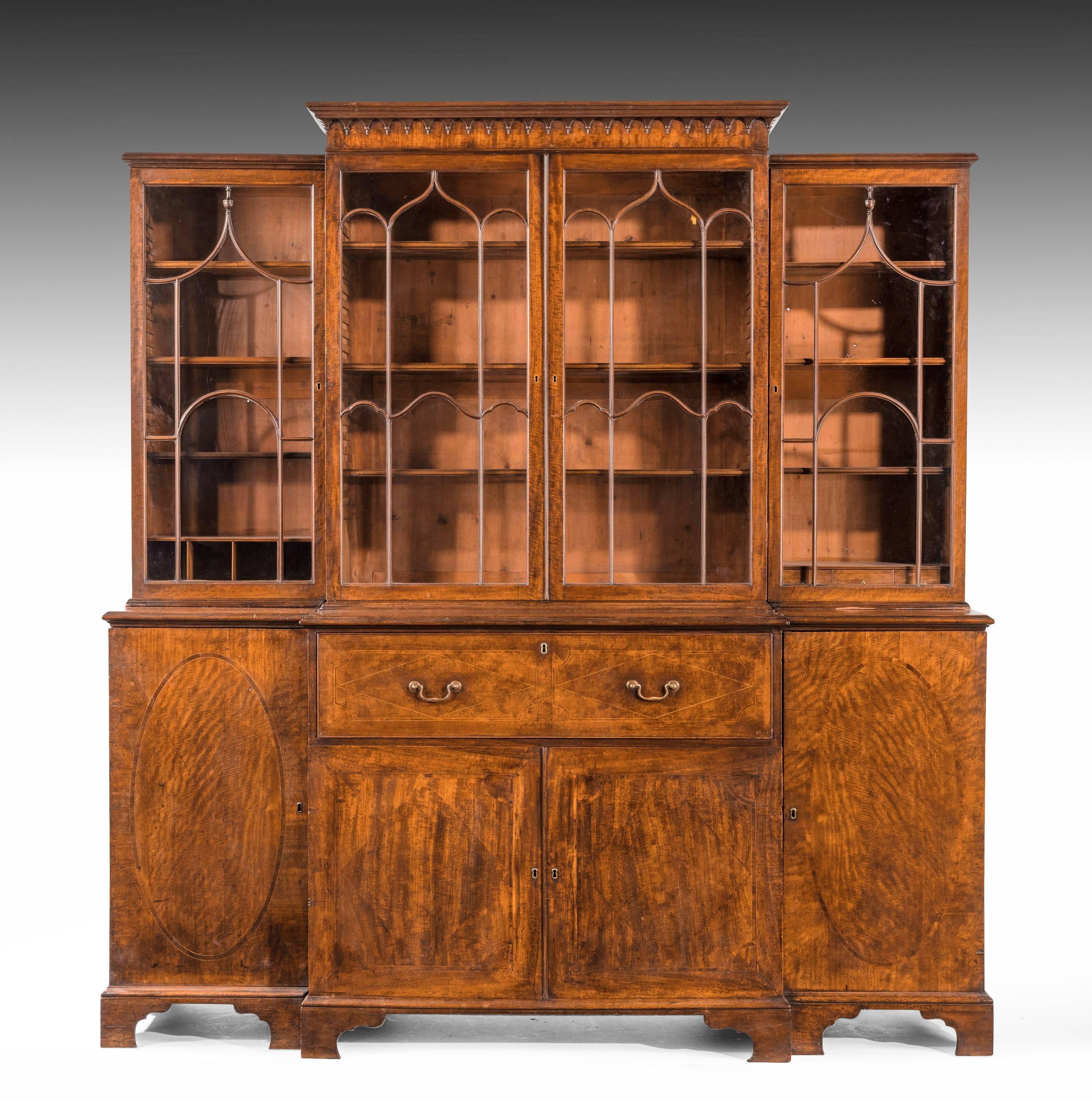 A handsome George III period mahogany breakfront bookcase. The outer doors with contrasting oval panels within quartered frames. The top with a finely carved dentil cornice. Original period bracket feet. Well fitted interior with drawers and pigeon
