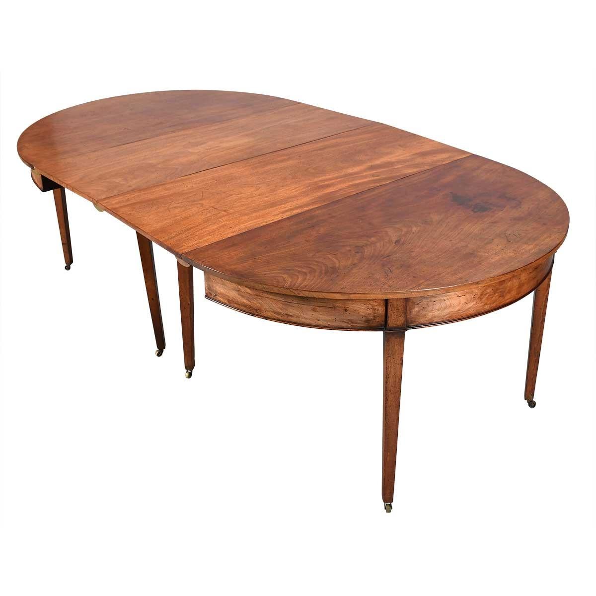A mahogany dining table on tapered legs raised on brass casters. The table is comprised of two demilune ends and two leaves. The back legs of the ends swing to support the leaves when used as a dining table. The ends also would make an attractive