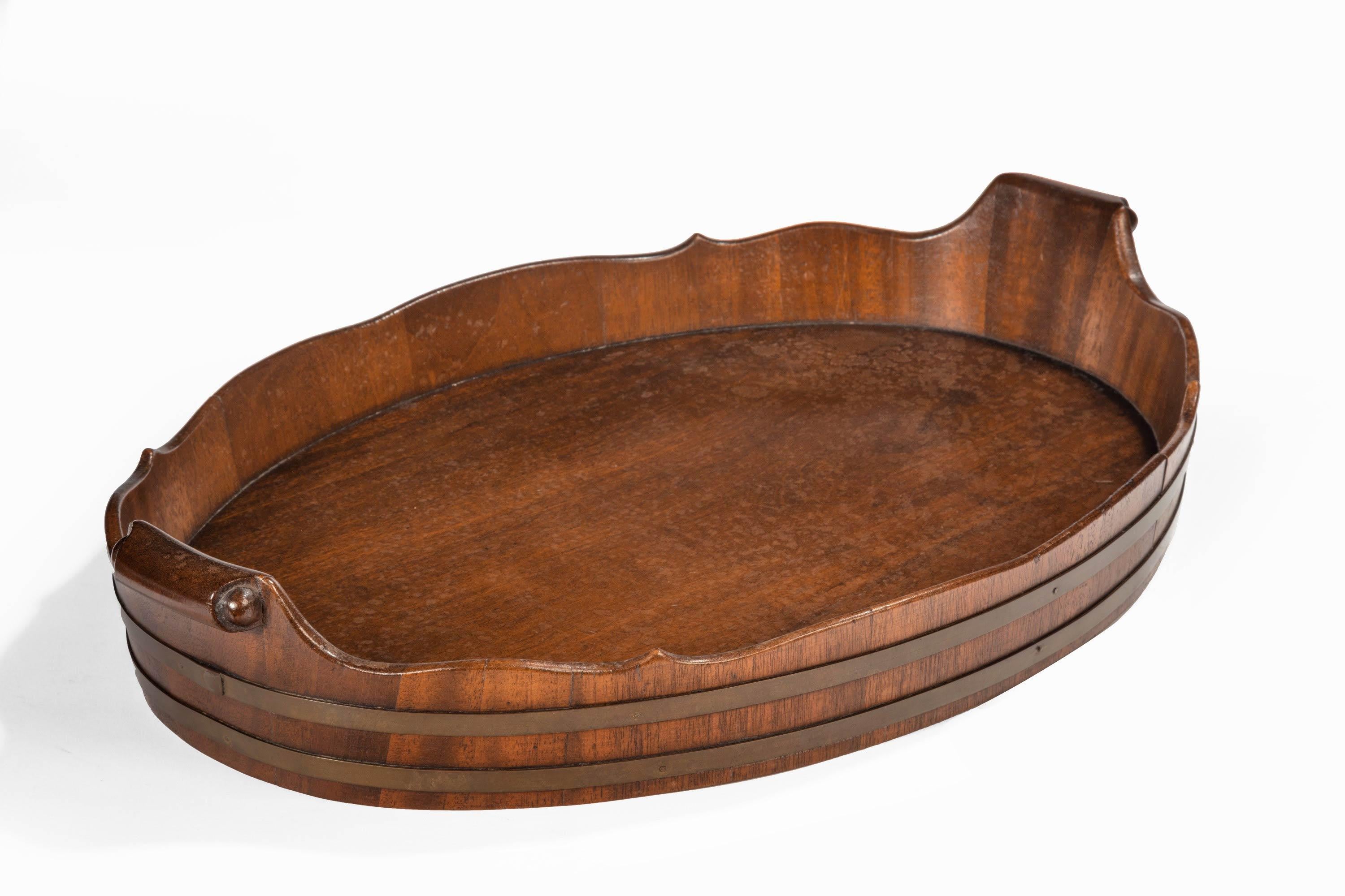 A very good George III period mahogany oval tray with an unusually deep border. Surmounted with two original brass bindings. Most attractive inlaid curled handles.