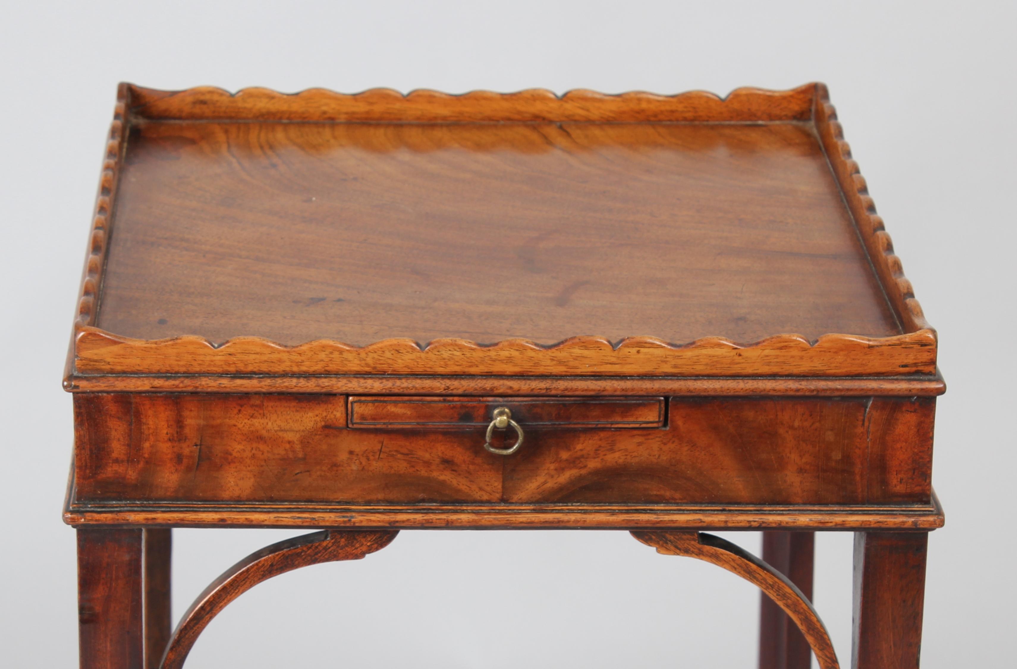 George III period mahogany urn-stand; the square top surrounded by scalloped gallery above a frieze fitted with a slide, on square legs with a shaped cross-stretcher.