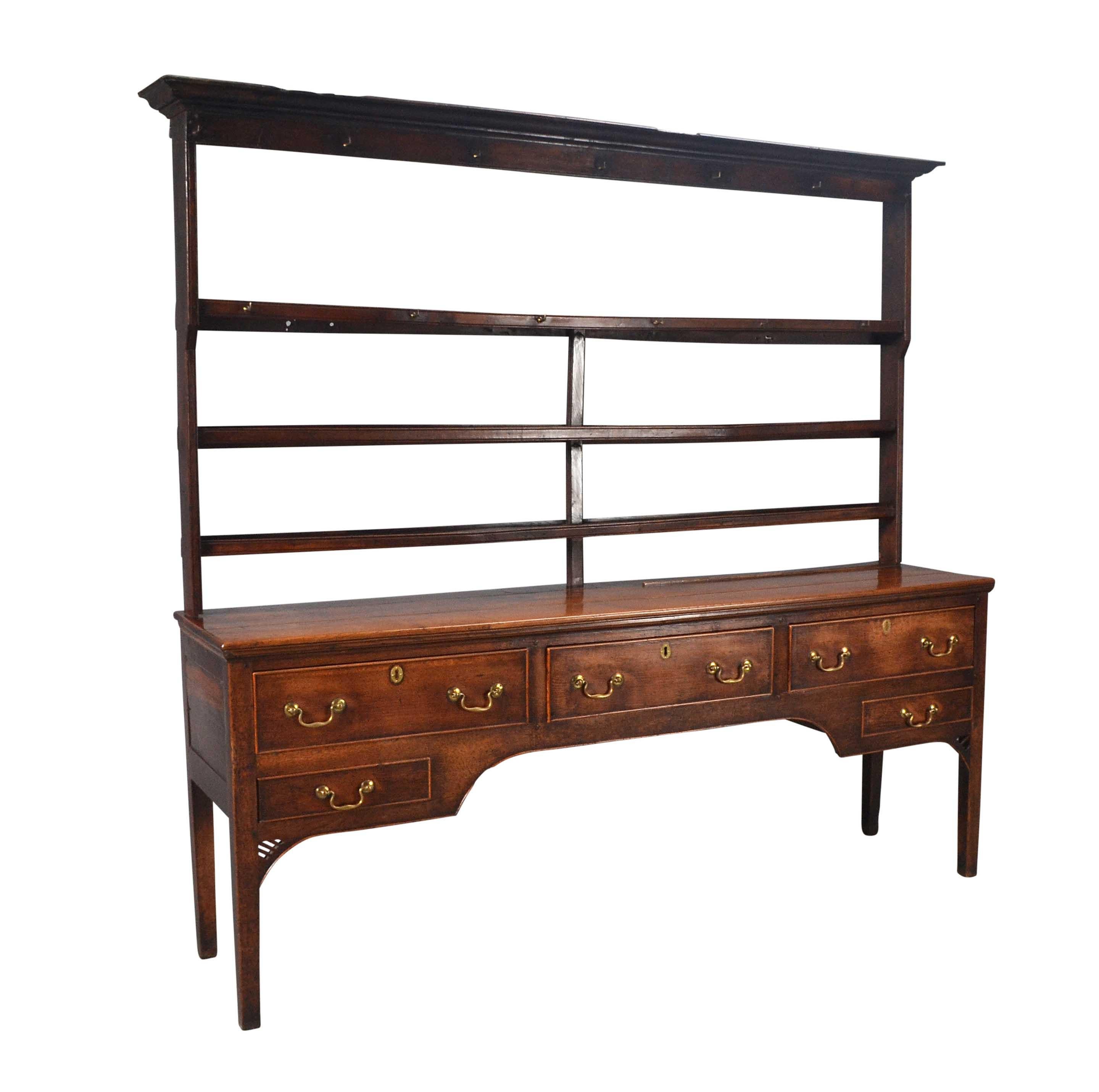 Comò e scaffale in Oak, con tre cassetti lunghi e due corti disposti intorno a un grembiule ad arco. In piedi, su gambe dritte sormontate da pennacchi traforati. Costruito con legname denso e di alta qualità. Il portapiatti è fissato con ganci per